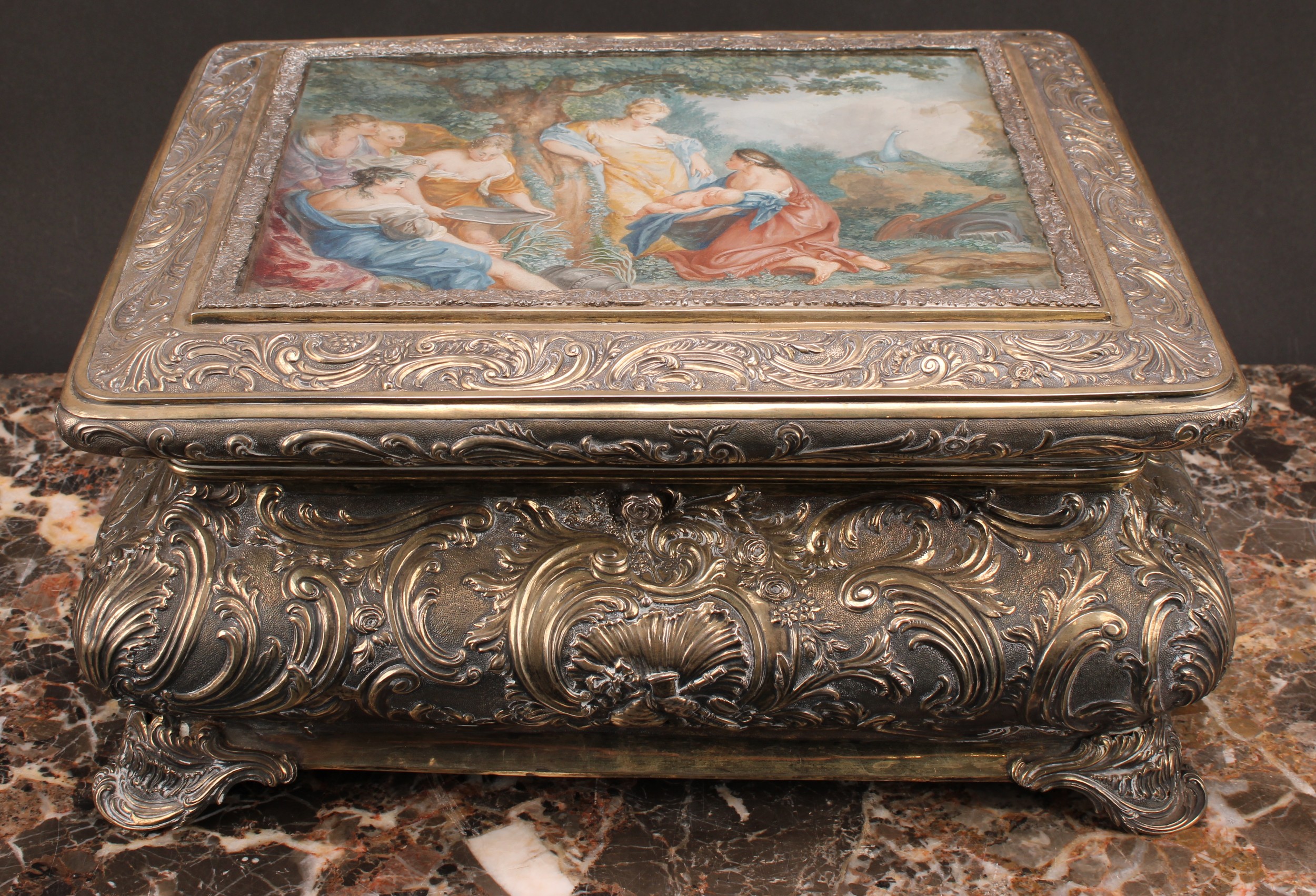 A 19th century German silver table casket, hinged cover with glazed top enclosing a gouache on paper depicting The Birth of Adonis in the manner of François Boucher, repoussé decorated throughout in the rococo taste with shells, flowers and scrolling foliage, bracket feet, Hanau pseudo-marks, 16.5cm high, 34cm wide, 28.5cm deep