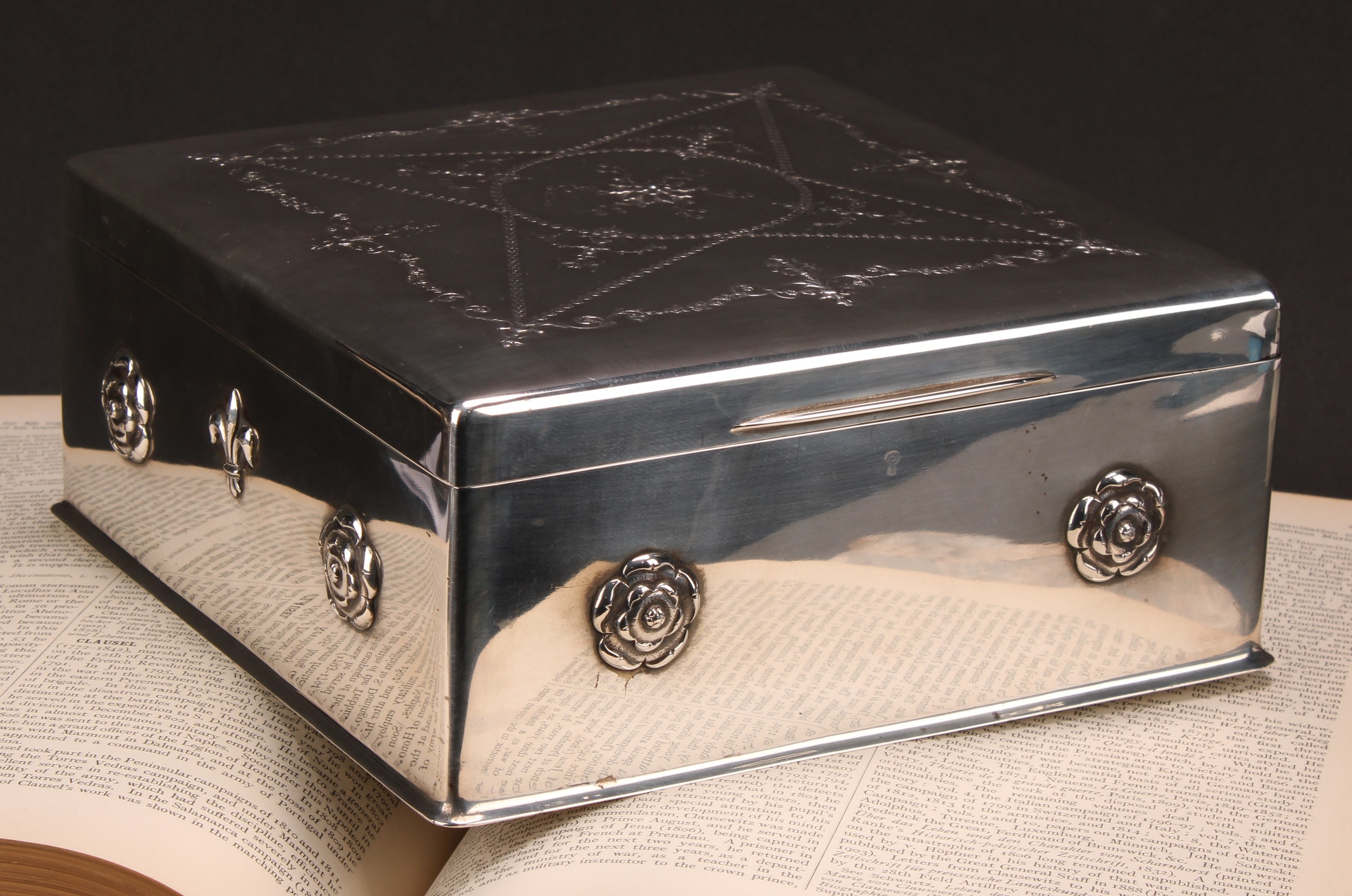An Edwardian silver square desk box, of substantial gauge, the hinged cover embossed with Neo-classical swags and foliate scrolls, the sides applied with rose and fleur-de-lys bosses, slightly spreading base, Frederick Haberling, London 1904, 2,005g