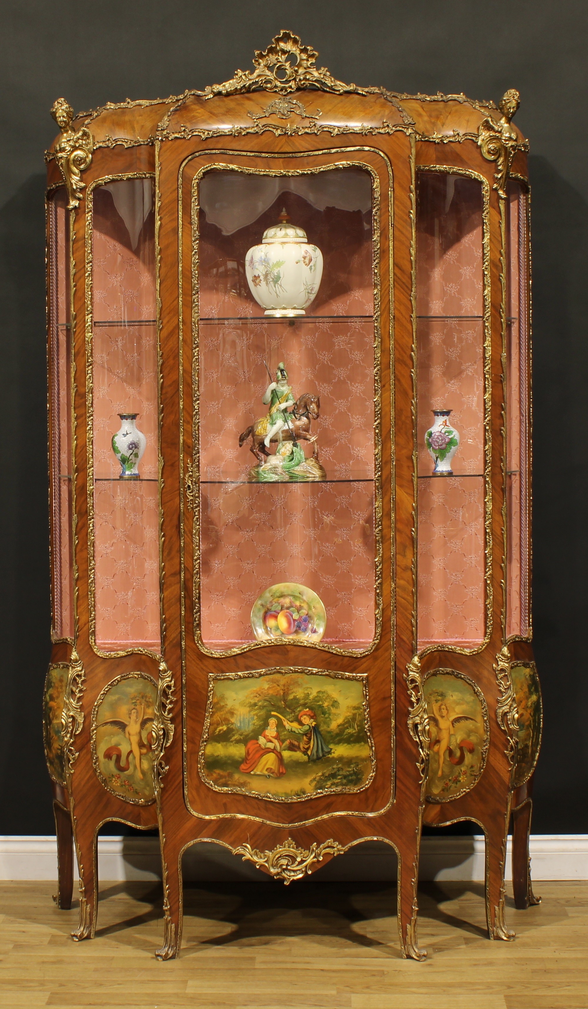 A large Louis XV Revival gilt metal mounted walnut and vernis Martin serpentine vitrine, three quarter glazed door flanked by glazed panels, the lower panels decorated with a courting couple, putti and landscapes, 213cm high, 125cm wide, 46cm deep, early 20th century