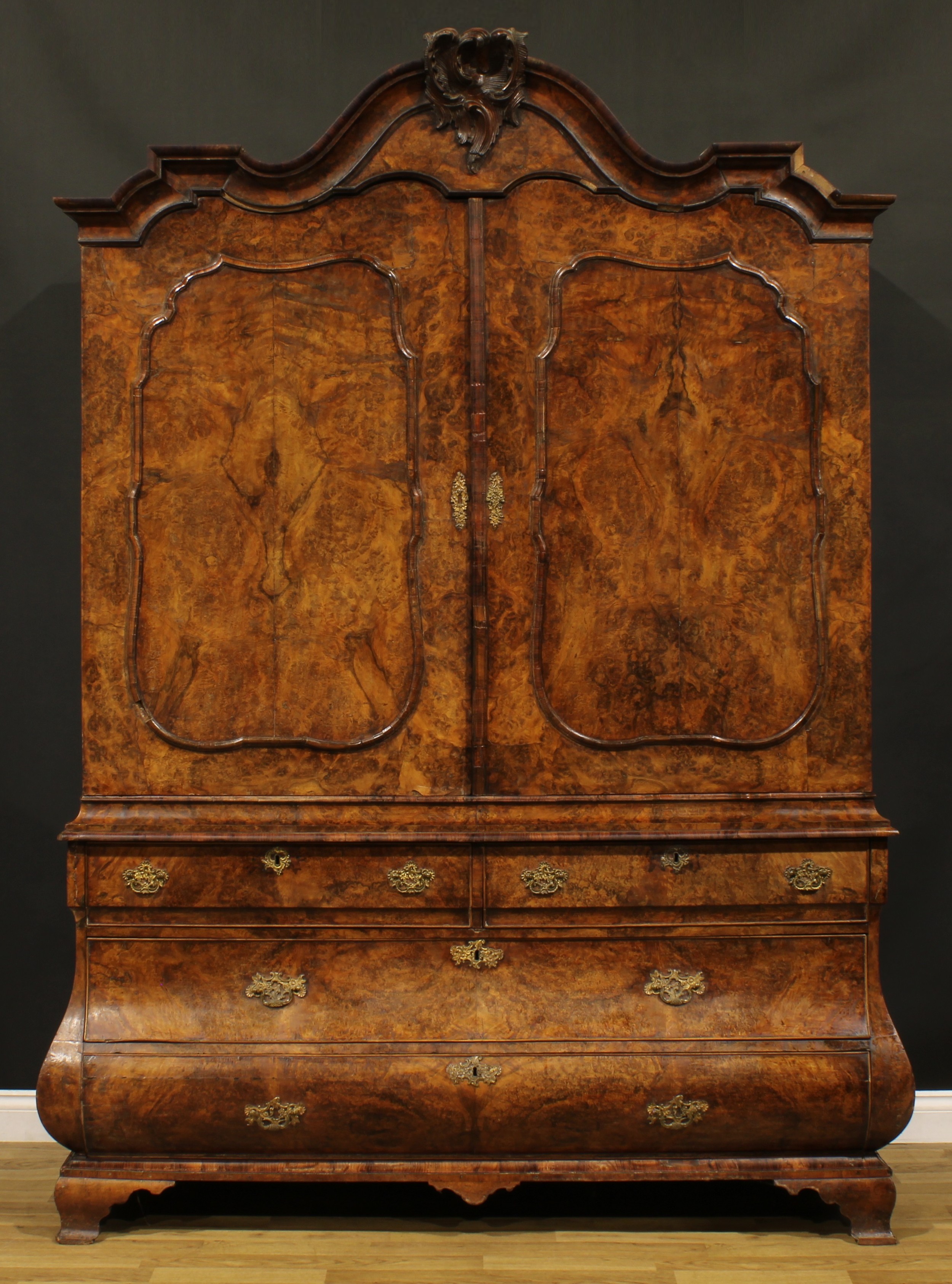 A large late 18th century Dutch burr walnut armoire or press cupboard, shaped chapeau de gendarme cresting above a pair of panel doors enclosing three shelves, the bombe shaped base with two short and two long drawers, ogee bracket feet, 241cm high, 173cm wide, 62cm deep, c.1790