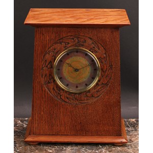 An Arts and Crafts oak mantel timepiece, 9cm circular dial decorated in mottled tones of orange and purple blush enamel, eight-day movement, the case with oversailing pediment, carved with a bezel band of swallows, bun feet, 26cm high, 21.5cm wide, c.1910