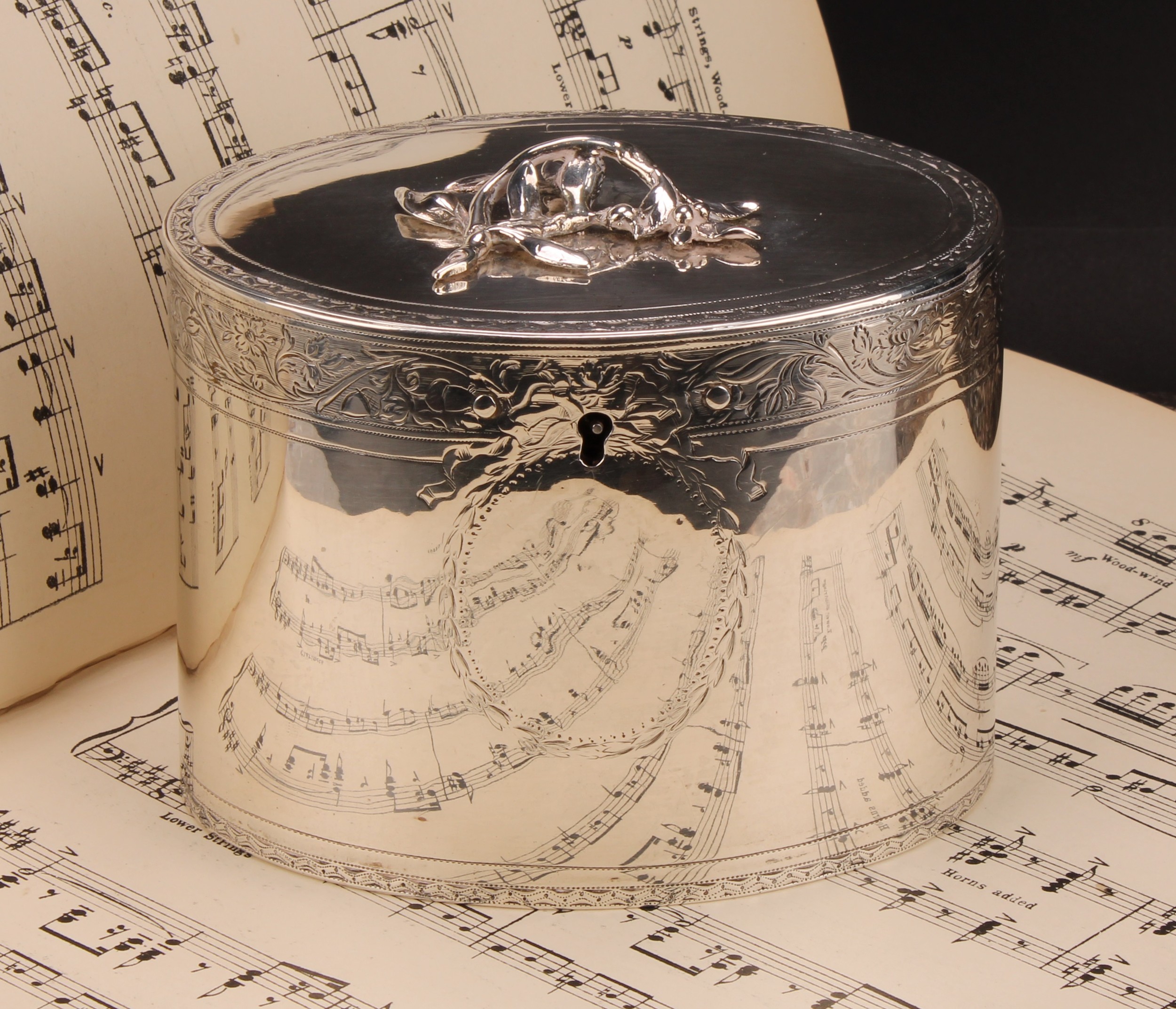 A George III silver oval tea caddy, flush-hinged cover with leafy branch finial, bright-cut engraved borders and vacant cartouche, 12.5cm wide, Augustus Le Sage, London 1774, 384g