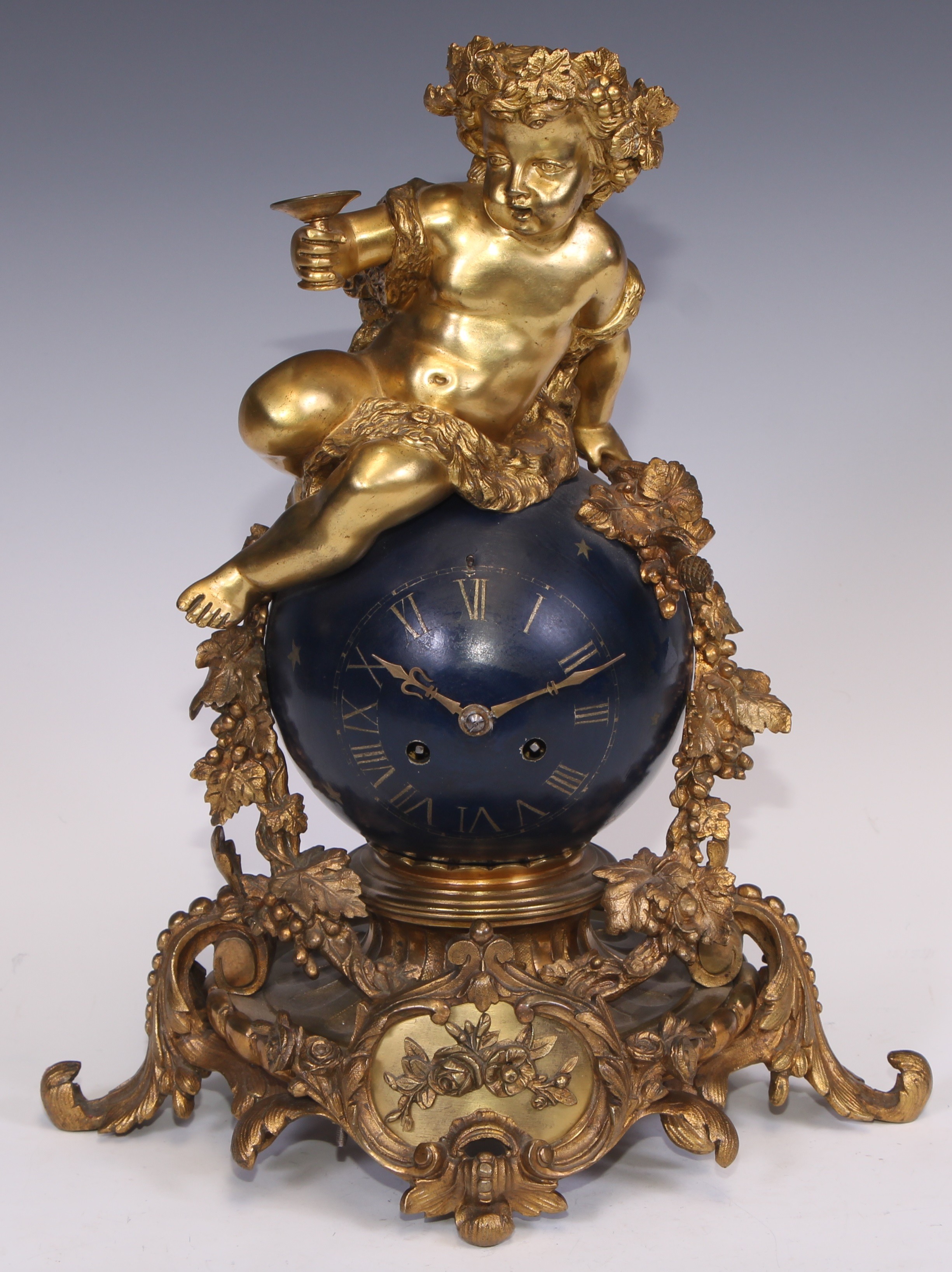 A Napoleon III ormolu and japanned mantel clock, cast as a Bacchic putto atop a celestial orb draped with fruiting vine, twin winding holes, eight-day movement by Rollin, Paris striking on a bell, acanthus scroll base, 35cm high, c.1860