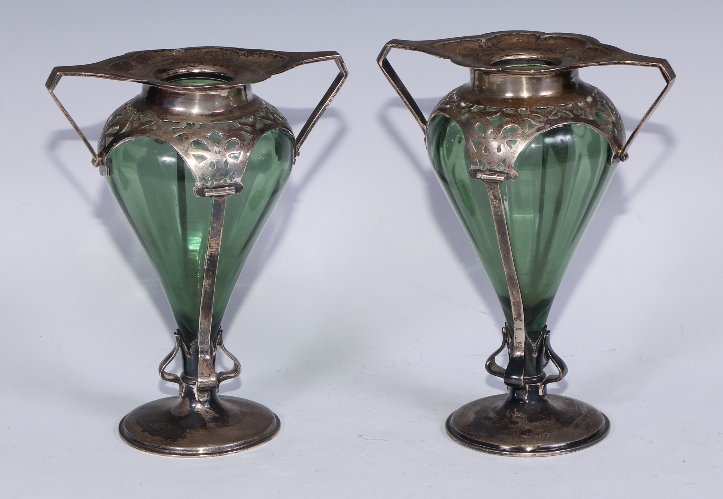 A pair of Art Nouveau silver mantel vases, canted angular handles, whiplash-pierced mounts, circilar bases, green glass liners, 18cm high, William Hutton & Sons Ltd, London 1903