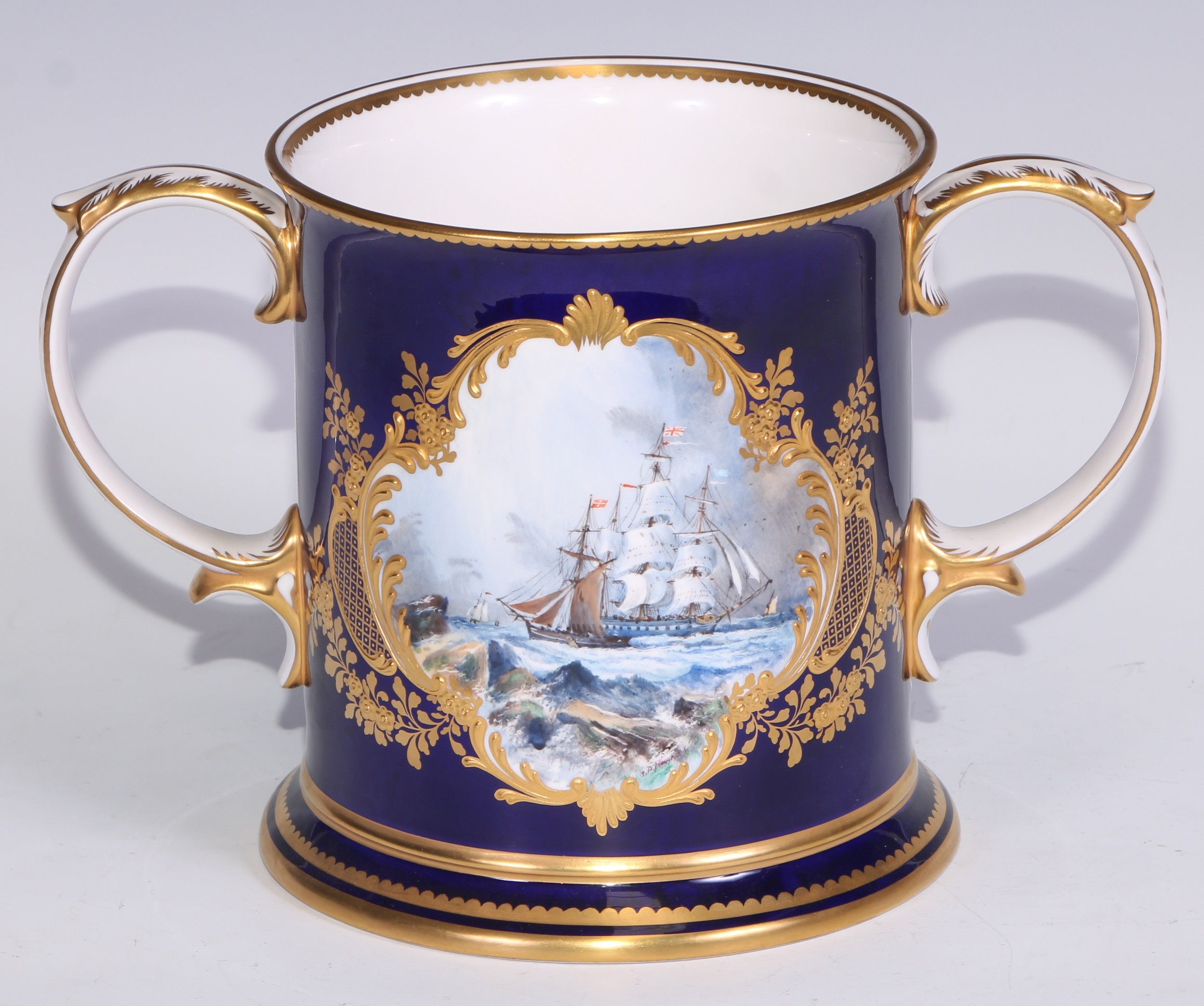 A large Lynton Porcelain Company loving cup, painted by Stefan Nowacki, signed, with a maritime scene of ships on a choppy sea,  gilded on a cobalt blue ground, 25cm over scroll-capped handles, printed marks and monogram