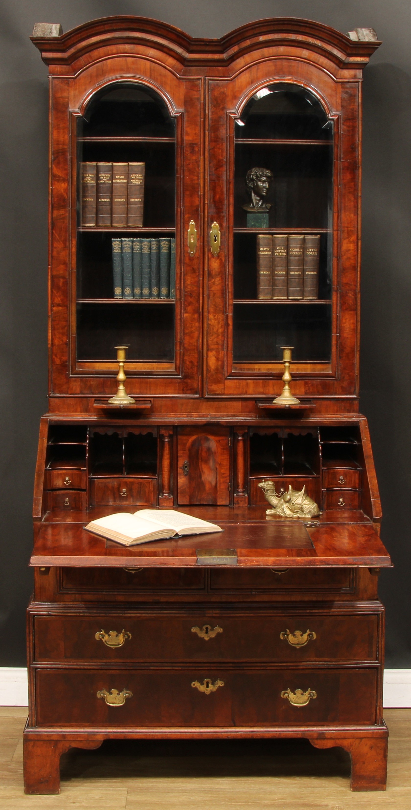 A Queen Anne walnut double dome bureau bookcase, outswept cornice above a pair of glazed doors enclosing three adjustable shelves and a pair of small drawers above two candle slides, the projecting base with a fall front door applied with a reading ledge and enclosing a writing surface, small door, small drawers, pigeonholes and secret compartments above a slide and a pair of short drawers, the base with two long drawers, bracket feet, 203cm high, 94.5cm wide, 56.5cm deep