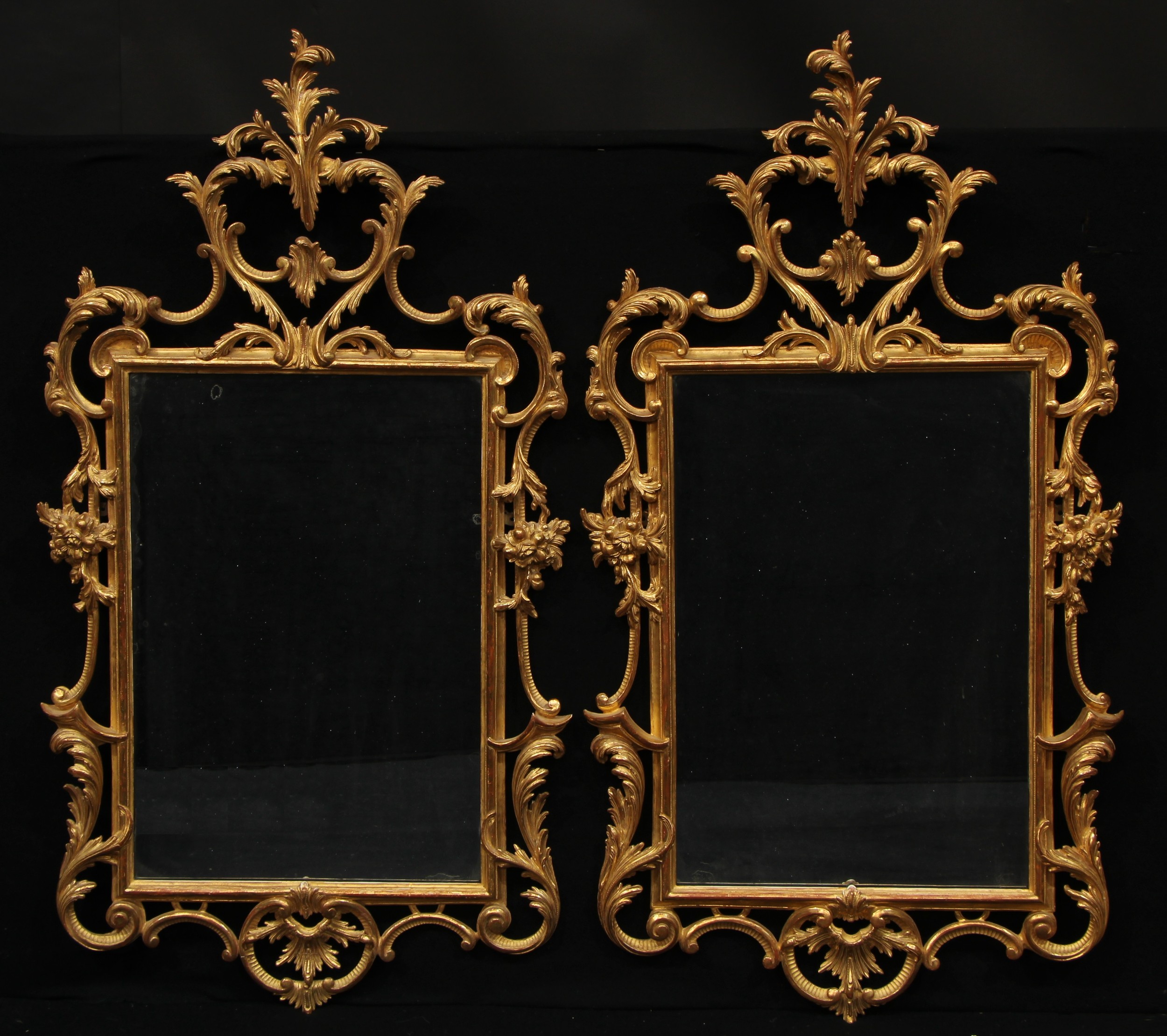 A pair of Rococo giltwood pier glasses, profusely carved and gessoed with scrolling acanthus, flowers and C-scrolls, rectangular mirror plates, 136cm high, 72cm wide