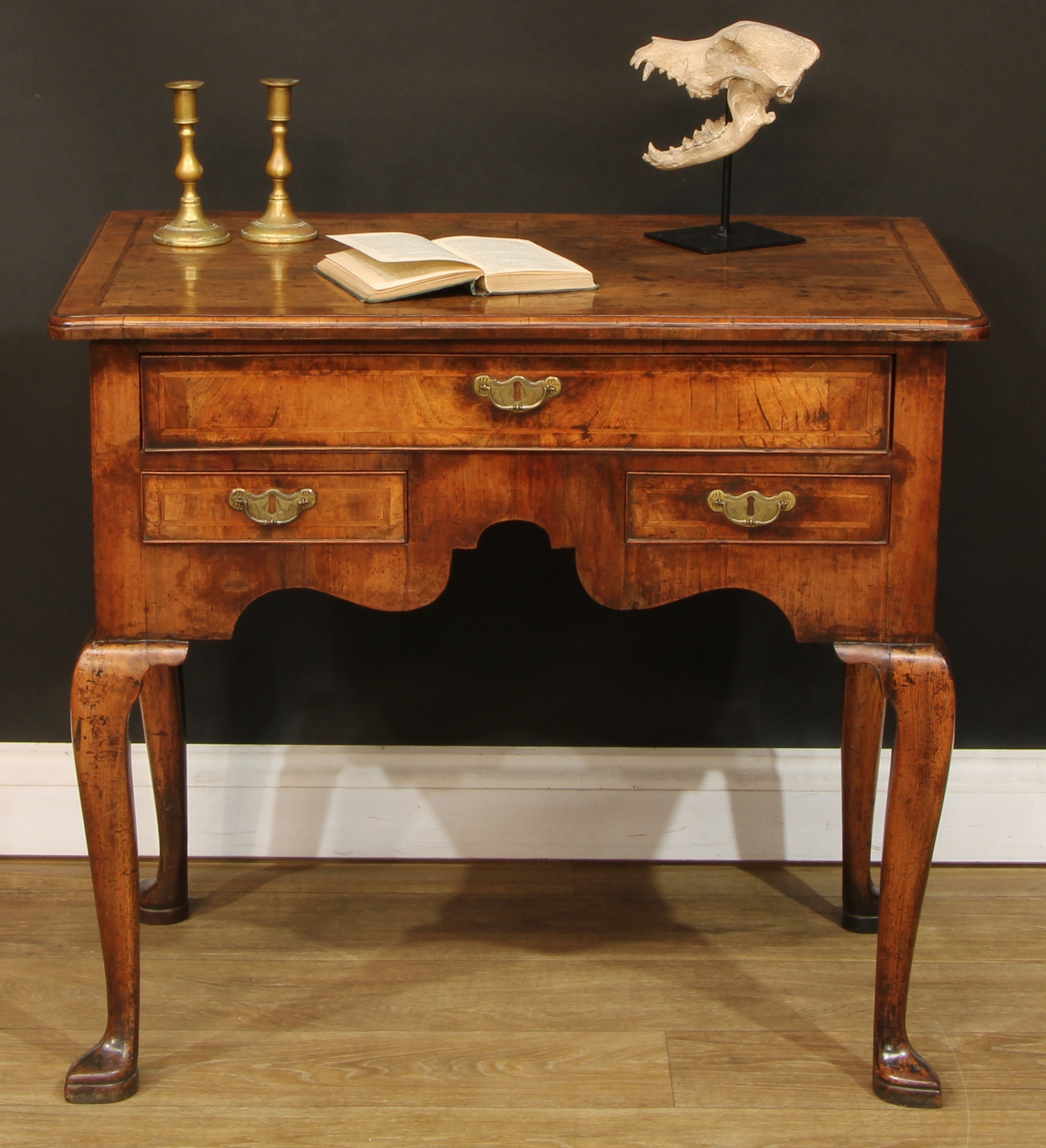 A George I featherbanded walnut lowboy or side table, crossbanded rectangular top above an arrangement of three cockbeaded drawers, shaped apron, cabriole legs, pointed pad feet, 71cm high, 80.5cm wide, 49.5cm deep, c.1720