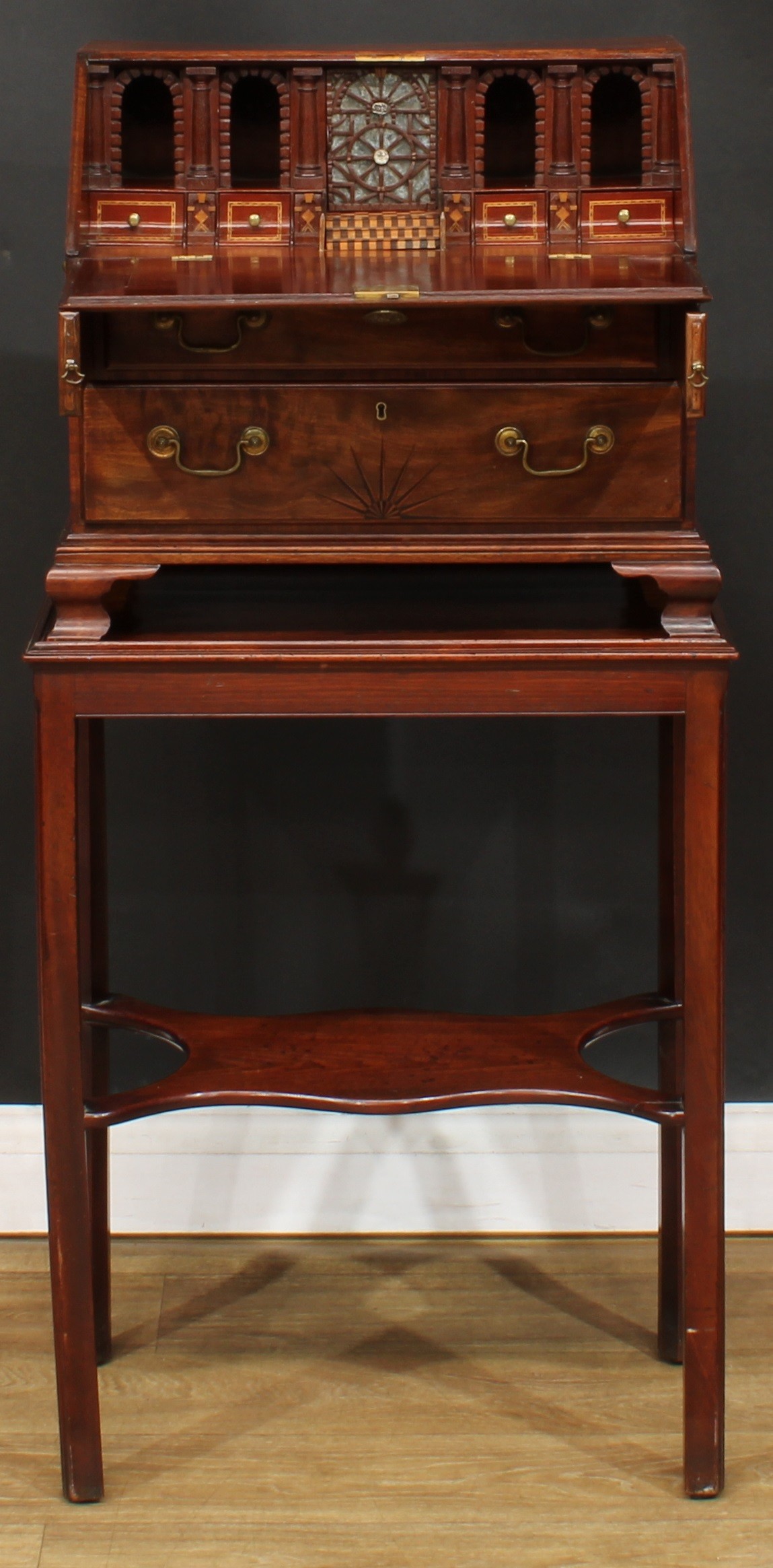 Miniature Furniture - a George III mahogany tabletop bureau, fall front enclosing a parquetry accented interior with a small fretwork mounted mirrored door, small drawers, rusticated niches and secret compartments, above two long graduated drawers, the lower inlaid in boxwood and ebony with a rising sun motif, carry handles to sides, skirted base, ogee bracket feet, the associated stand with moulded and internally chamfered square legs, open undertier, the bureau 43.5cm high, 50.5cm wide, 28.5cm deep, the stand 68.5cm high, 53cm wide, 32.5cm deep