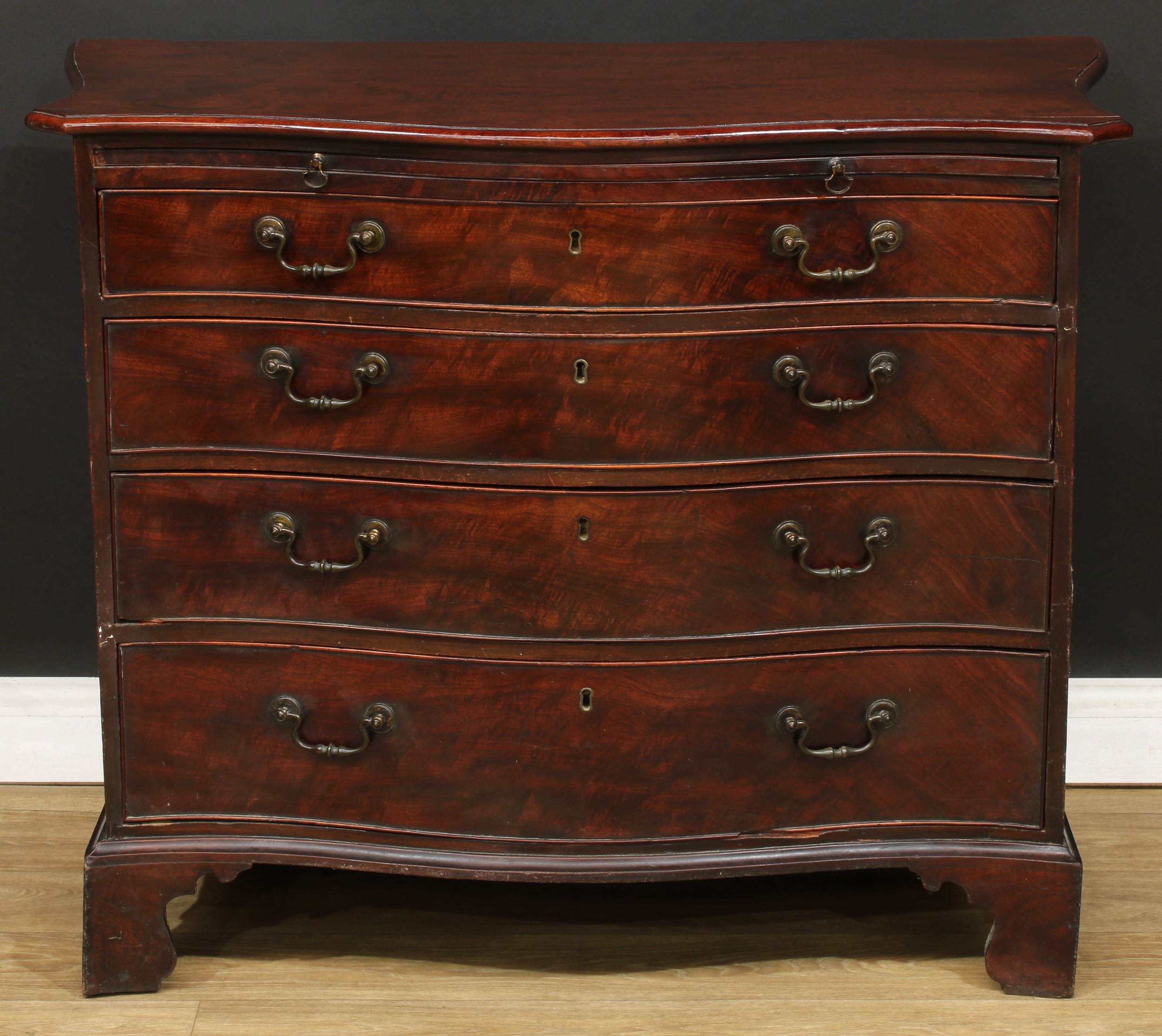 A George III mahogany serpentine bachelor’s chest, oversailing top above a slide and four long graduated drawers, bracket feet, 83cm high, 104cm wide, 52.5cm deep, c.1780