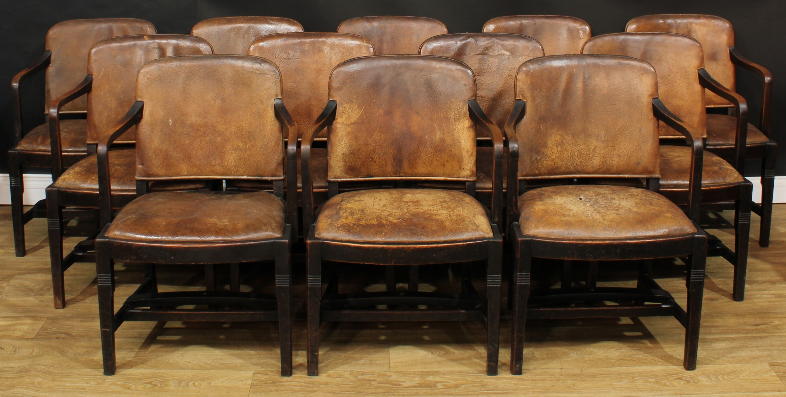 A set of twelve Art Deco oak and leather club elbow chairs, possibly by Hamptons, Pall Mall East, London, bearing label to underside AFT SMOKE ROOM, the stretcher stencilled E/BRITAIN or remnants thereof, purportedly removed from the luxurious steam turbine ocean liner RMS Empress of Britain prior to her being torpedoed on the 28 October 1940, probably removed prior to 25 November 1939 as she was requisitioned as a troop transporter, 83.5cm high, 57cm wide, the seat 48cm wide and 37cm deep, c.1925