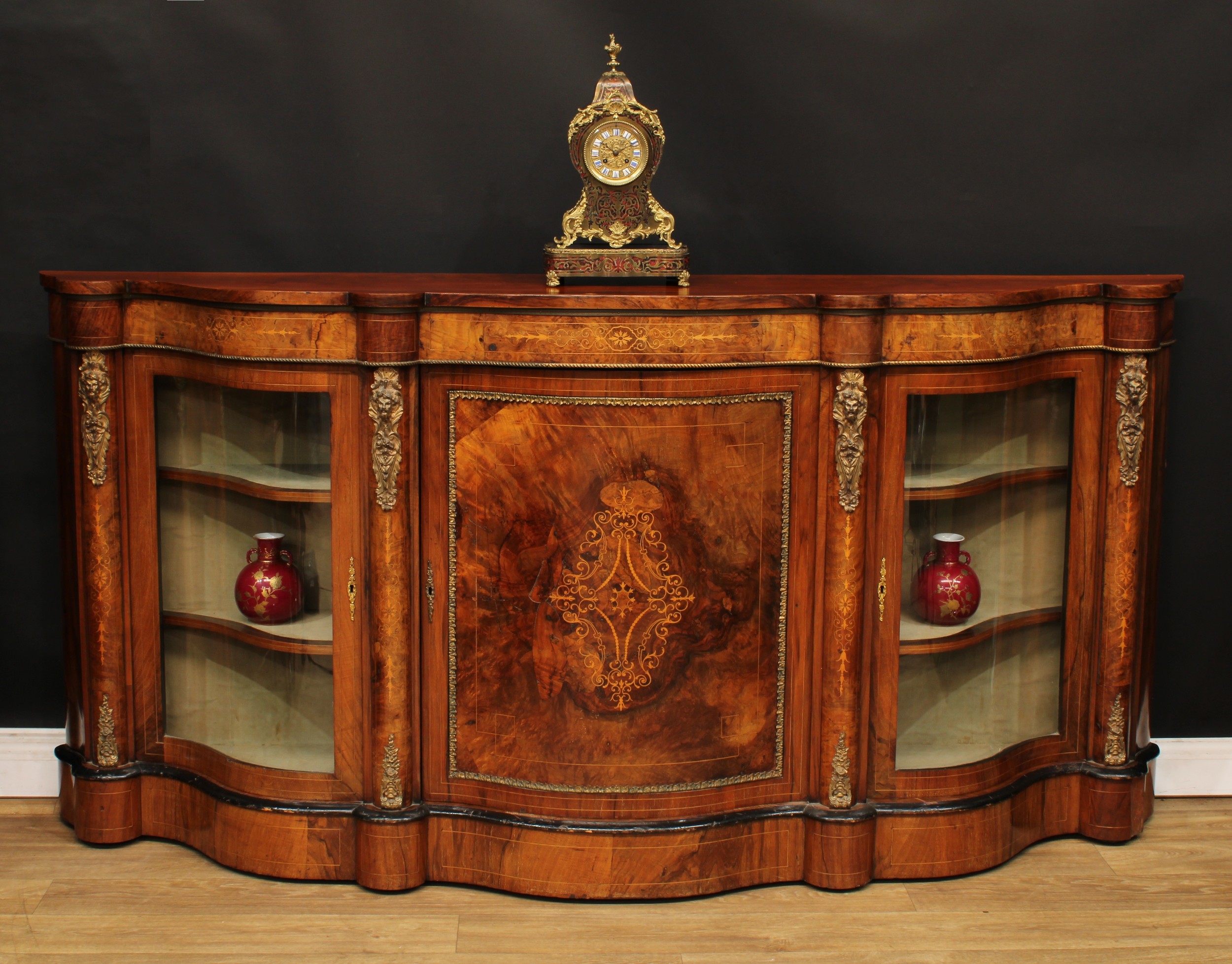 A Victorian gilt metal mounted walnut and marquetry serpentine credenza, slightly oversailing top above a panel door inlaid with scrolling leaves flanked by glazed vitrine doors, plinth base, 104cm high, 211.5cm wide, 46cm deep, c.1870
