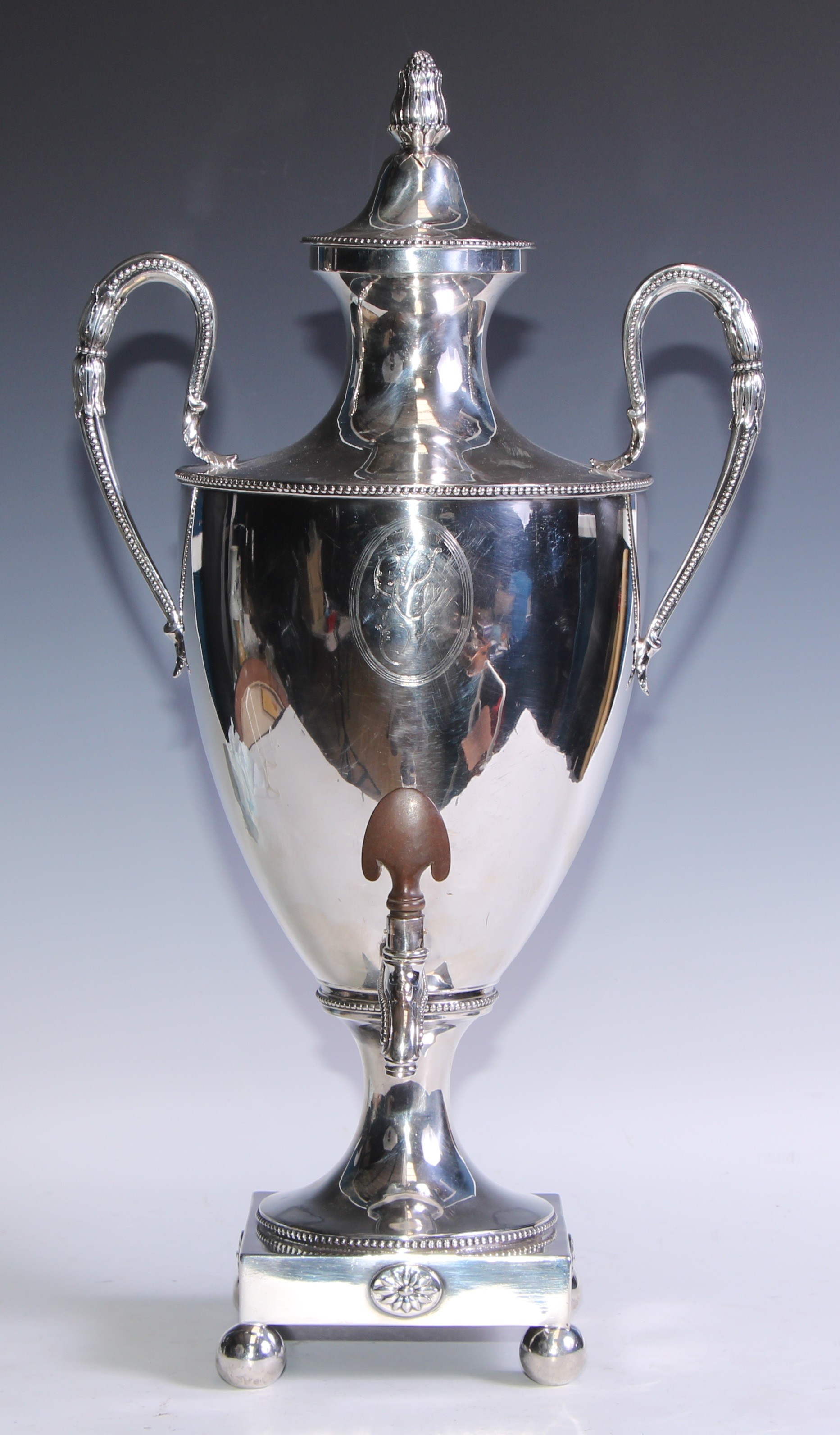 A George III silver urnular pedestal samovar or tea urn, in the Robert Adam taste, bud finial, acanthus grasped beaded scroll handles, square base applied with oval sunflower paterae, beaded borders, ball feet, 53cm high, Henry Green, London 1777, 2516g