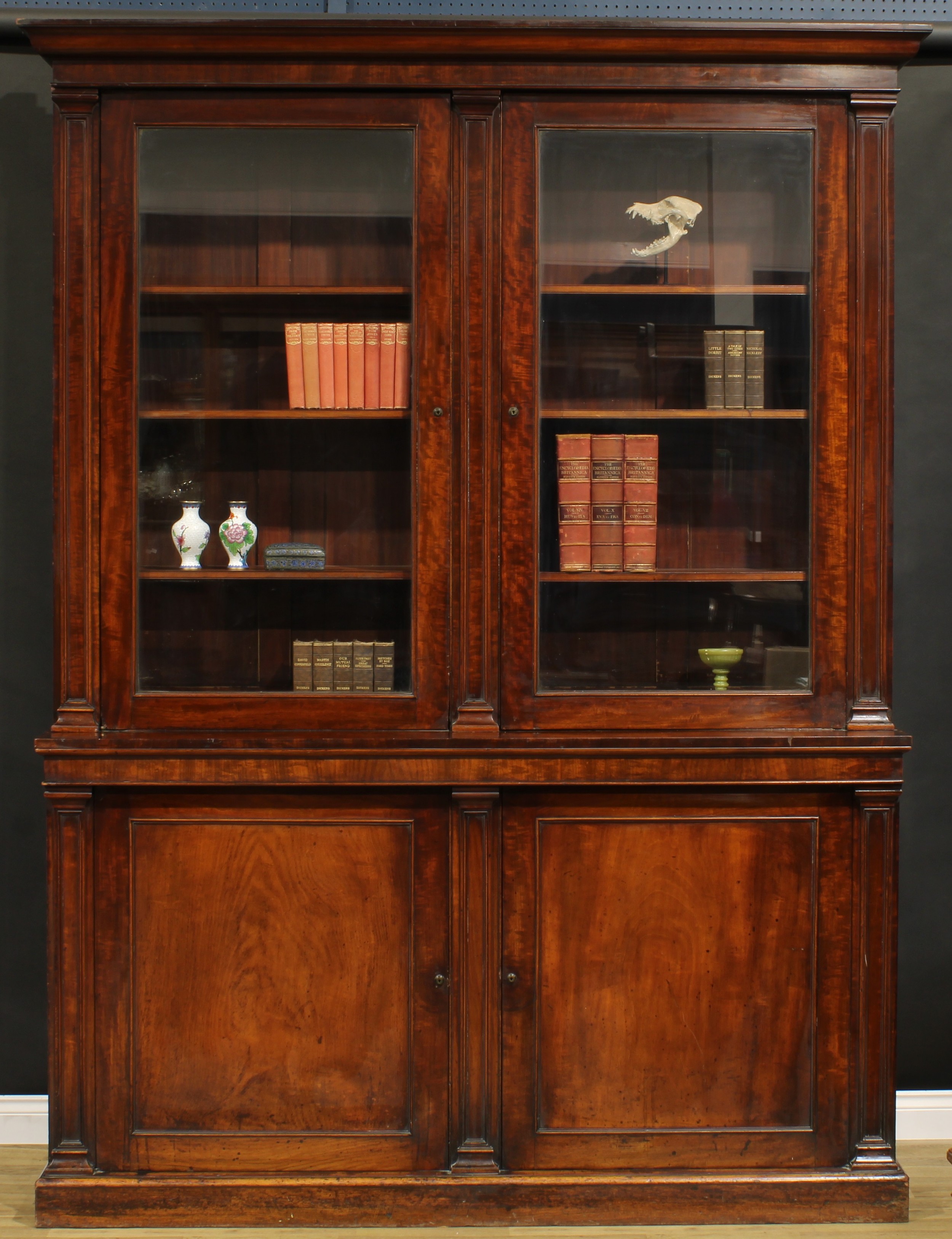 A Post-Regency mahogany library bookcase, outswept cornice above a pair of glazed doors enclosing adjustable shelves, the projecting base with a pair of panel doors, Bramah locks, plinth base, 262cm high, 199.5cm wide, 46.5cm deep