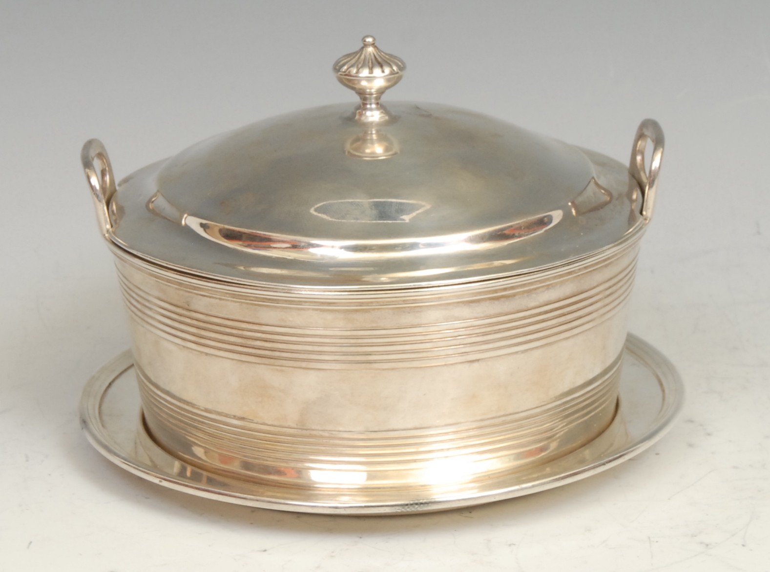 A George III silver circular butter dish, cover and stand, fluted knop finial, lug handles above two reeded bands, glass liner, 14cm diam, Rebecca Emes & Edward Barnard I, London 1813, 496g