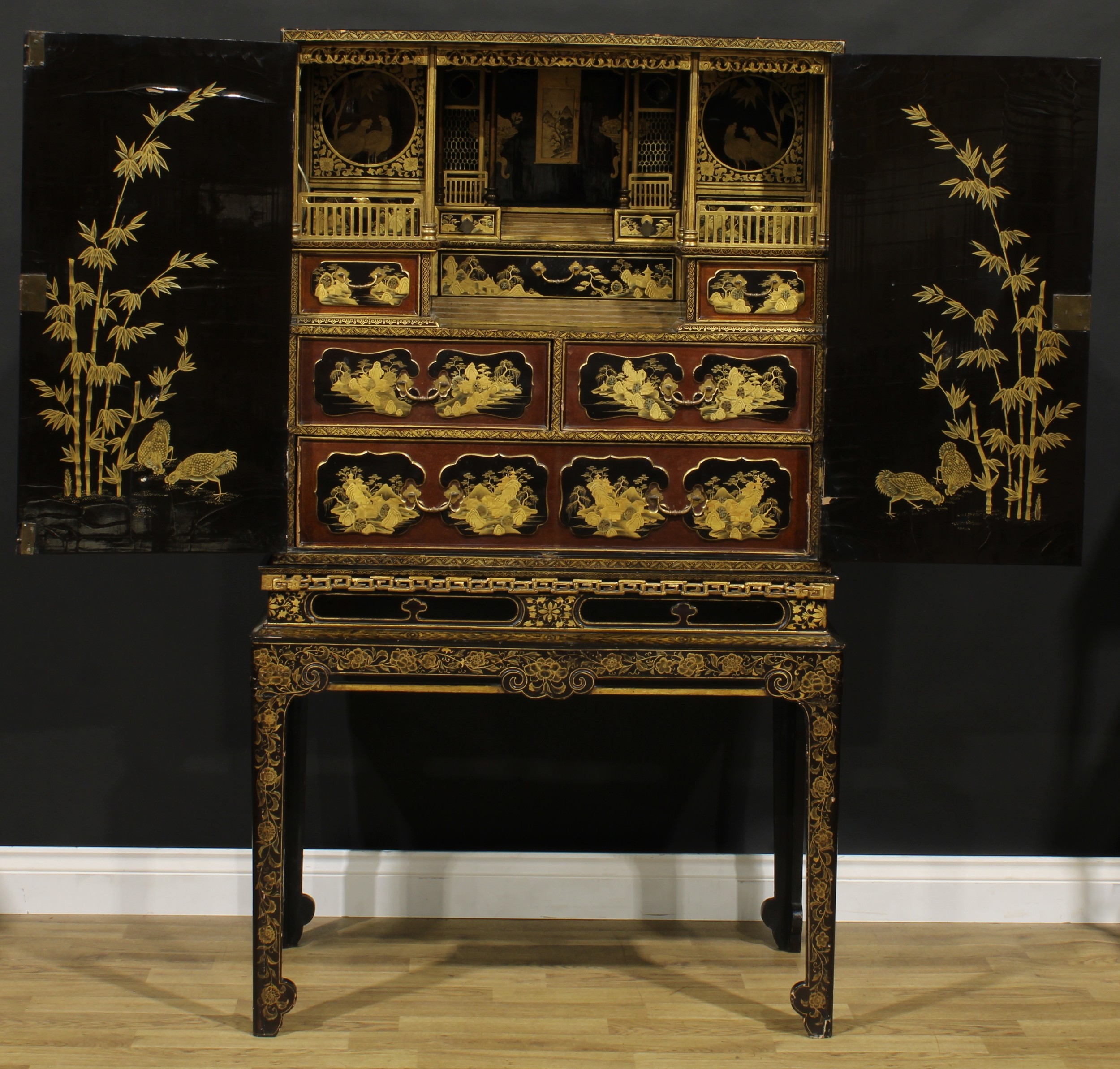 An 18th century Revival Chinese export lacquer enclosed cabinet, decorated throughout in gilt with traditional landscape scenes, enclosing an architectural interior with drawers and niches, 156.5cm high, 92cm wide, 54cm deep