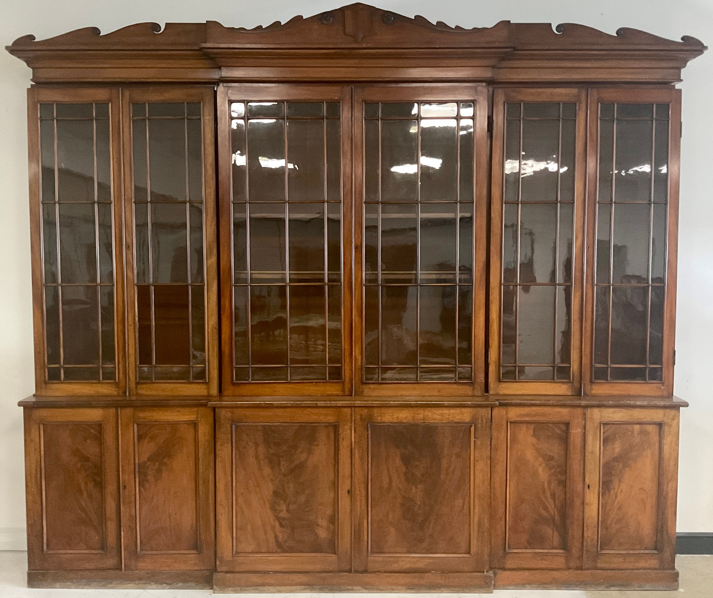 A large early Victorian mahogany break-centre library bookcase, shaped wavy cresting centred by a shield shaped reserve and applied with draught-turned roundels, above an arrangement of doors, 330cm wide, c.1840