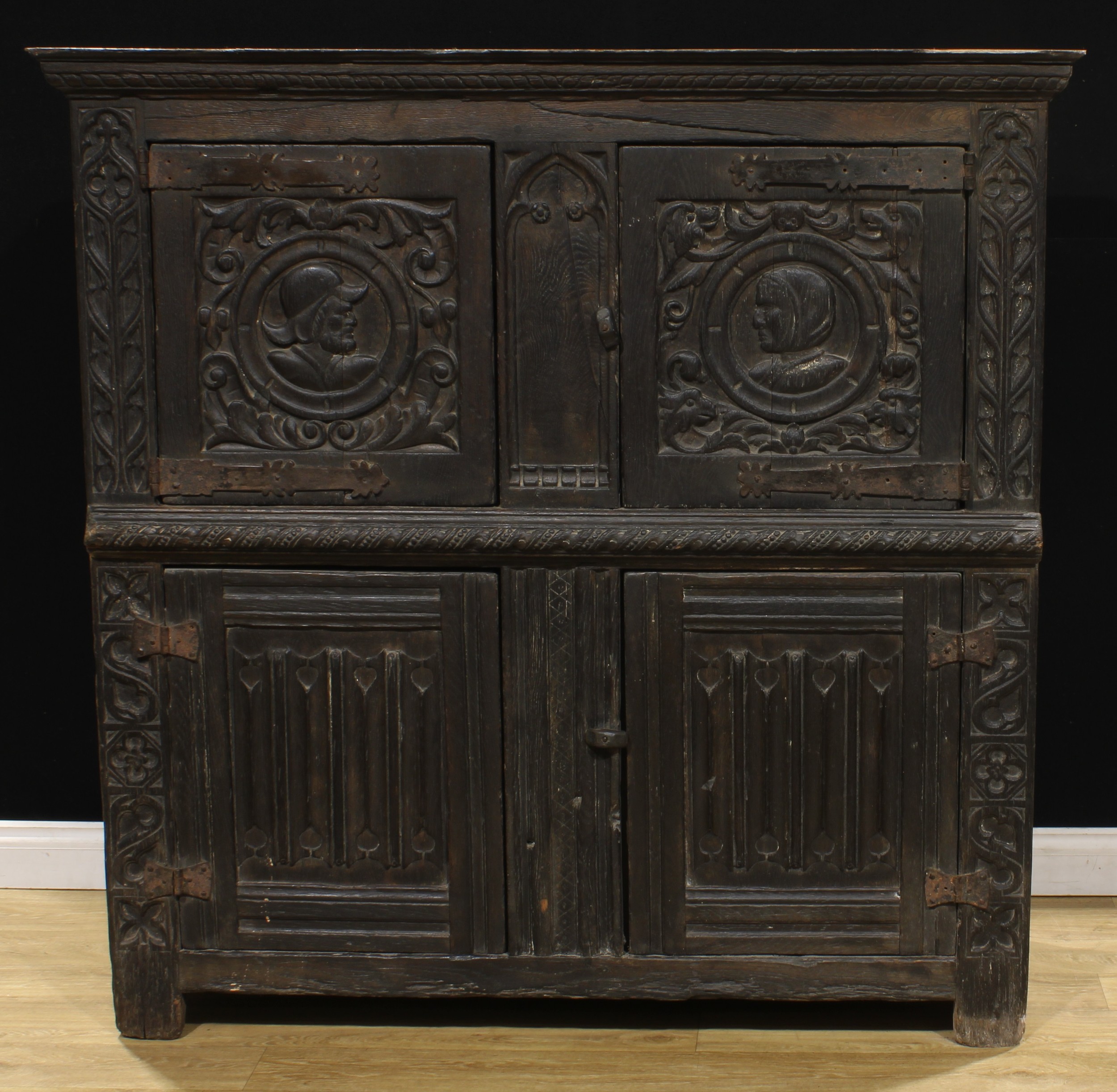 A 16th century French oak Romayne panel food cupboard, oversailing top above a pair of doors carved with opposing portraits in the typical Renaissance manner, the lower door panels carved with linenfolds, the angles carved with Gothic tracery, 147cm high, 147.5cm wide, 54.5cm deep, c.1550-1600