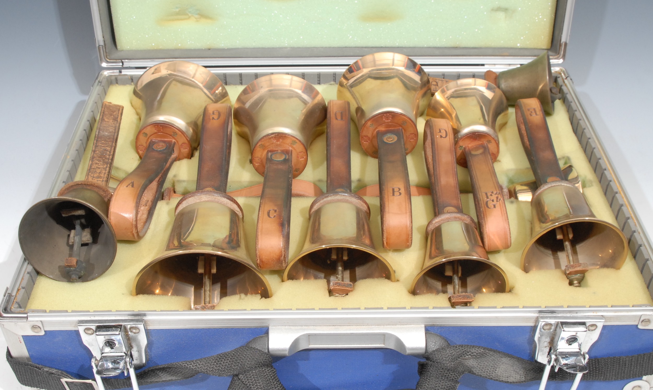 A set of ten brass hand bells, by The Whitechapel Bell Foundry, the G 21cm to top of leather strap, cased; two others (12)