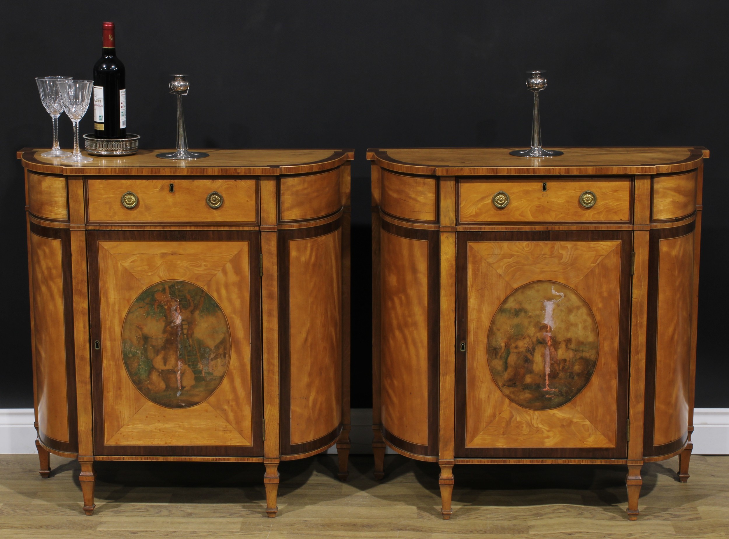 A pair of Sheraton Revival tulipwood banded satinwood side cabinets, each with a slightly oversailing top above a frieze drawer and a door, enclosing a shelf, square legs, 82.5cm high, 81cm wide, 35.5cm deep, c.1900