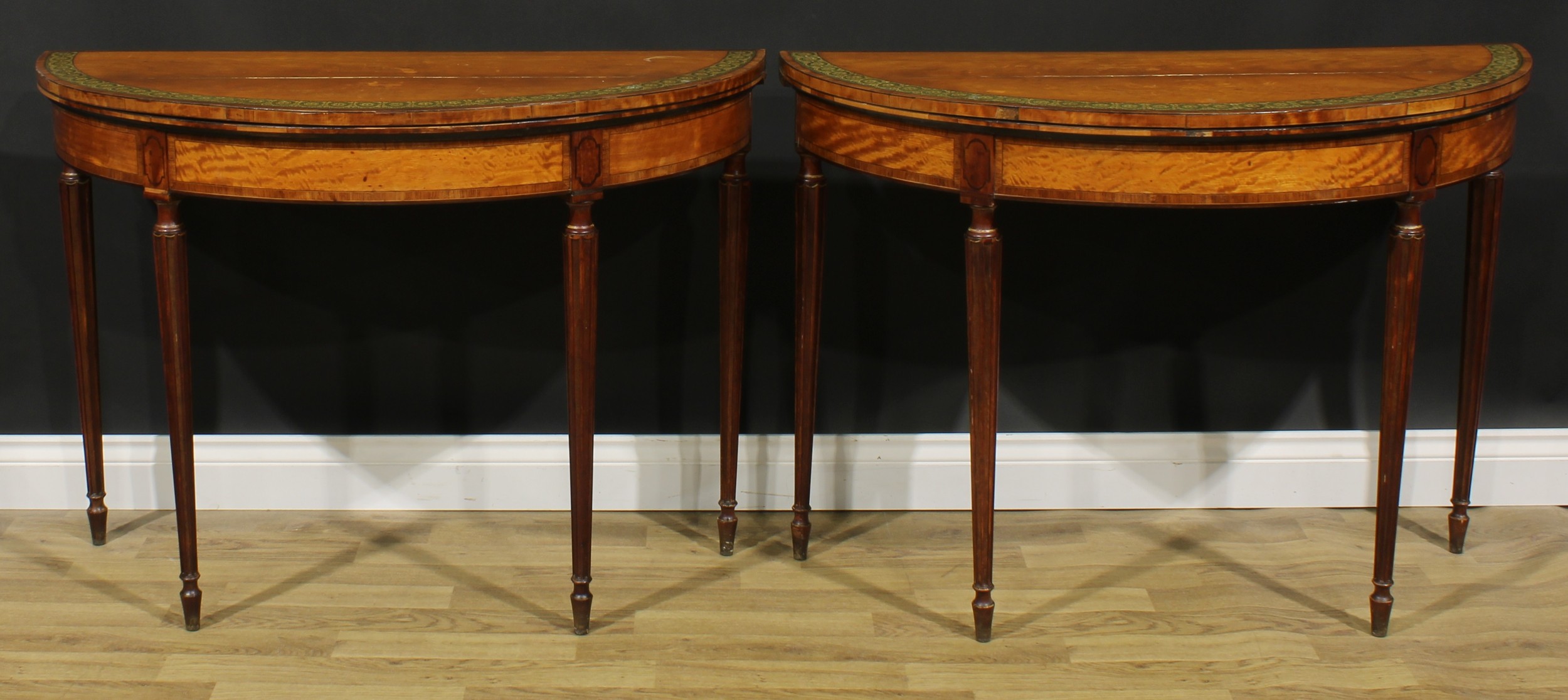 A pair of Sheraton period tulipwood crossbanded satinwood and painted demilune card tables, each with a hinged top enclosing a baize lined playing surface, fluted tapered octagonal legs, turned feet, 75.5cm high, 106.5cm wide, 48.5cm deep, c.1795