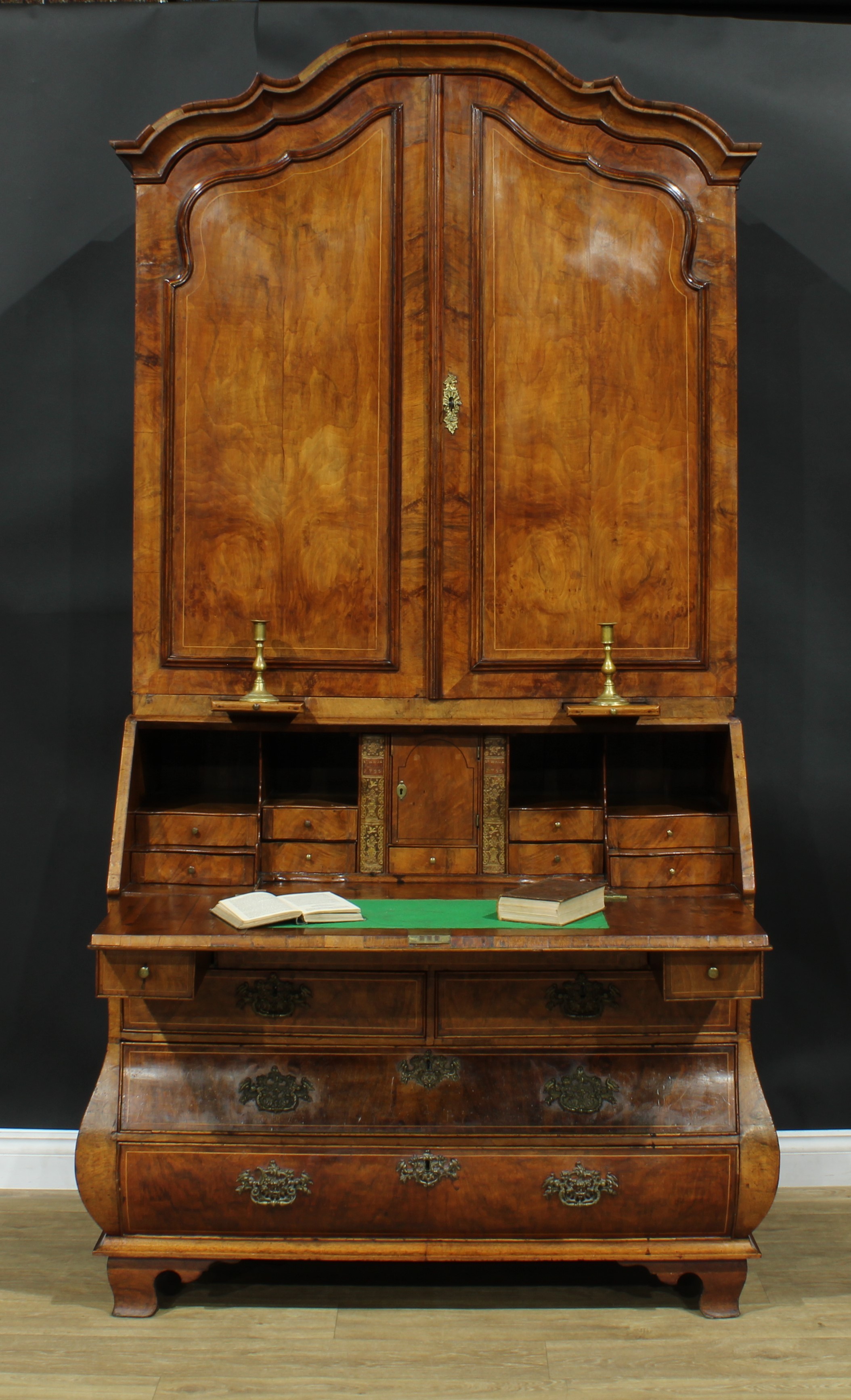 An 18th century Dutch walnut bureau book cabinet, the pair of panel doors above two candle slides and enclosing three adjustable shelves and three small drawers, the projecting base with fall front enclosing a well, a small door, small drawers, pigeonholes and secret compartments, above two short and two long drawers, skirted base, bracket feet, 230.5cm high, 122.5cm wide, 61cm deep