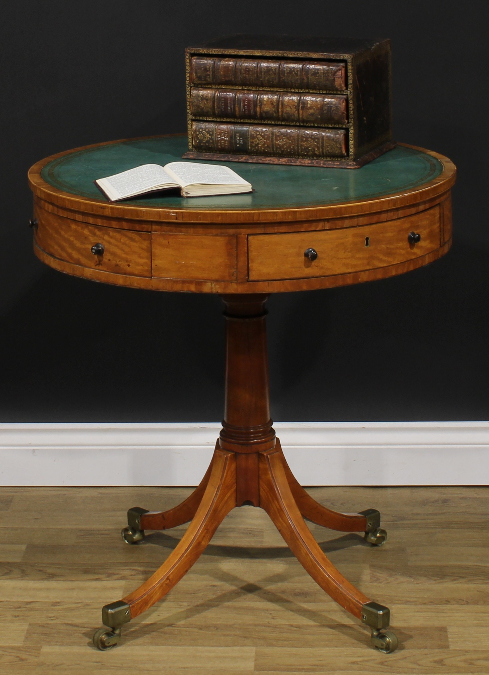 A Sheraton period satinwood drum table, tulipwood crossbanded top with inset tooled and gilt writing surface, turned column, sabre legs, brass capped casters, 71.5cm high, 67cm diameter, c.1795