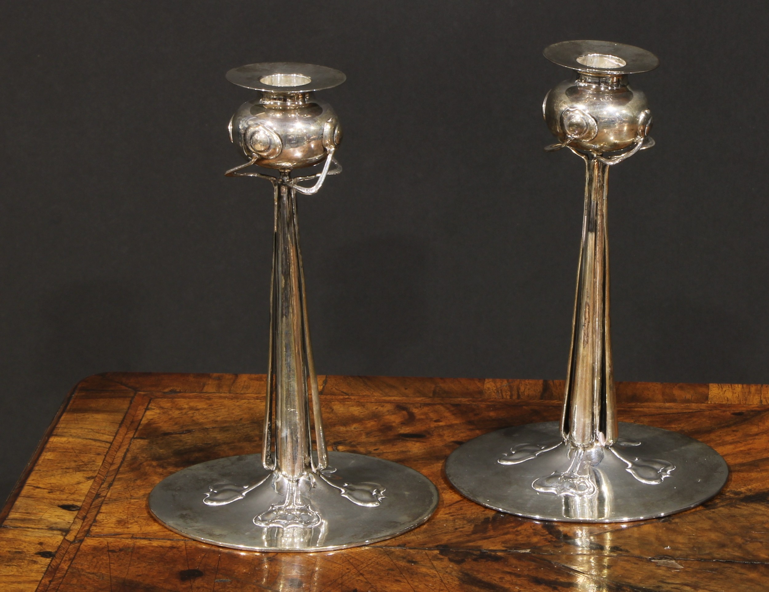 Liberty & Co - a pair of Arts and Crafts silver Cymric candlesticks, designed by by Archibald Knox (1864 - 1933), in the Art Nouveau taste with stylised organic forms, broad circular bases, 20cm high, Birmingham 1901