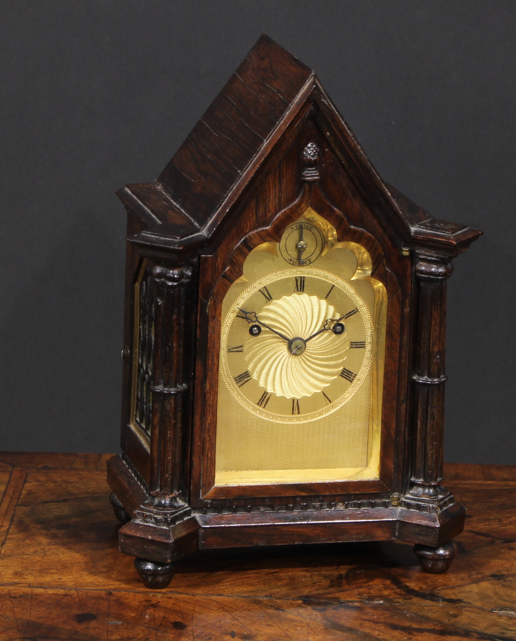 A George/William IV Gothic Revival rosewood bracket clock, of small almost carriage proportions, 8cm gilt engine turned dial inscribed with a chapter of Roman numerals, Strike/Silent to arch, twin-winding holes, English fusee movement striking on a bell, the pointed arched case flanked by cluster columns, knop feet, 25cm high, c.1830