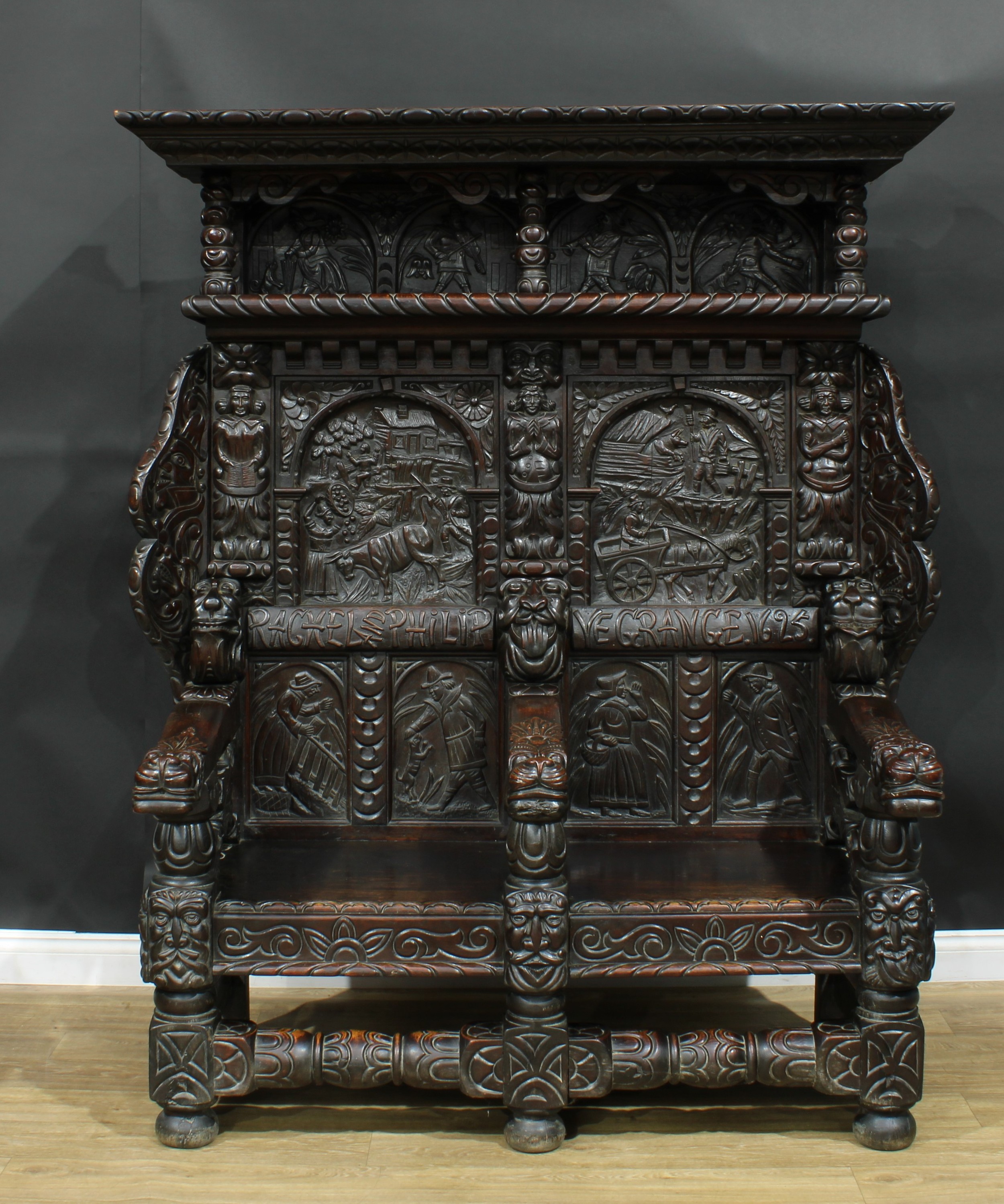 A large 17th century style oak settle, carved throughout with native folk scenes, grotesque masks and stylised leaves and flowers, 190.5cm high, 161cm wide, 80cm deep