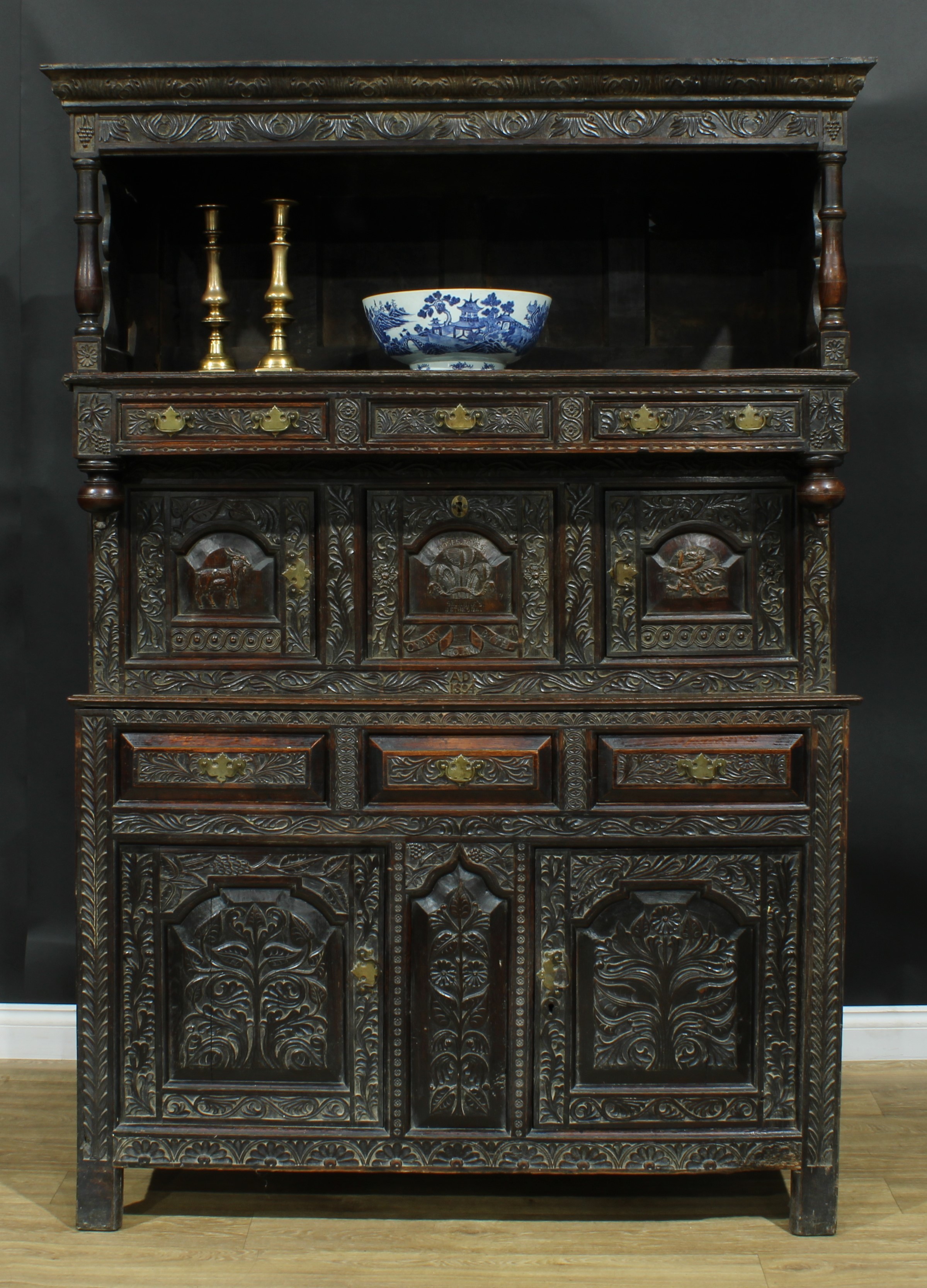 An 18th century and later oak tridarn, outswept cornice above a niche and an arrangement of drawers and doors, carved throughout with leaves and geometric motifs, the central doors carved with a goat, the Welsh Dragon and the Prince of Wales's feathers, inscribed CARVED BY MOSES JONES ST. ANNE’S BETHESDA, CYMRY FO AM BYTH, AD 1894, stile feet, 198cm high, 139.5cm wide, 50cm deep  Provenance - Sir John Kyffin Williams, OBE, RA sale, lot 299, 25JUN2007