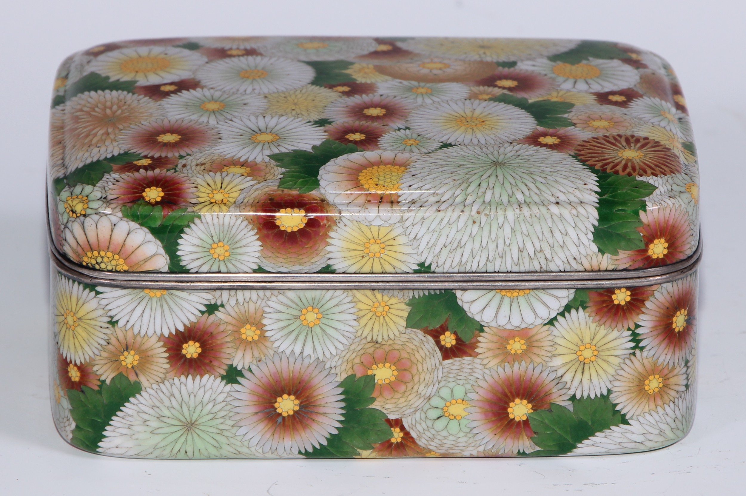 A Japanese cloisonne enamel rounded rectangular box and cover, decorated overall in polychrome with layered flowerheads, silver coloured metal mounts, 14cm wide, Meiji period