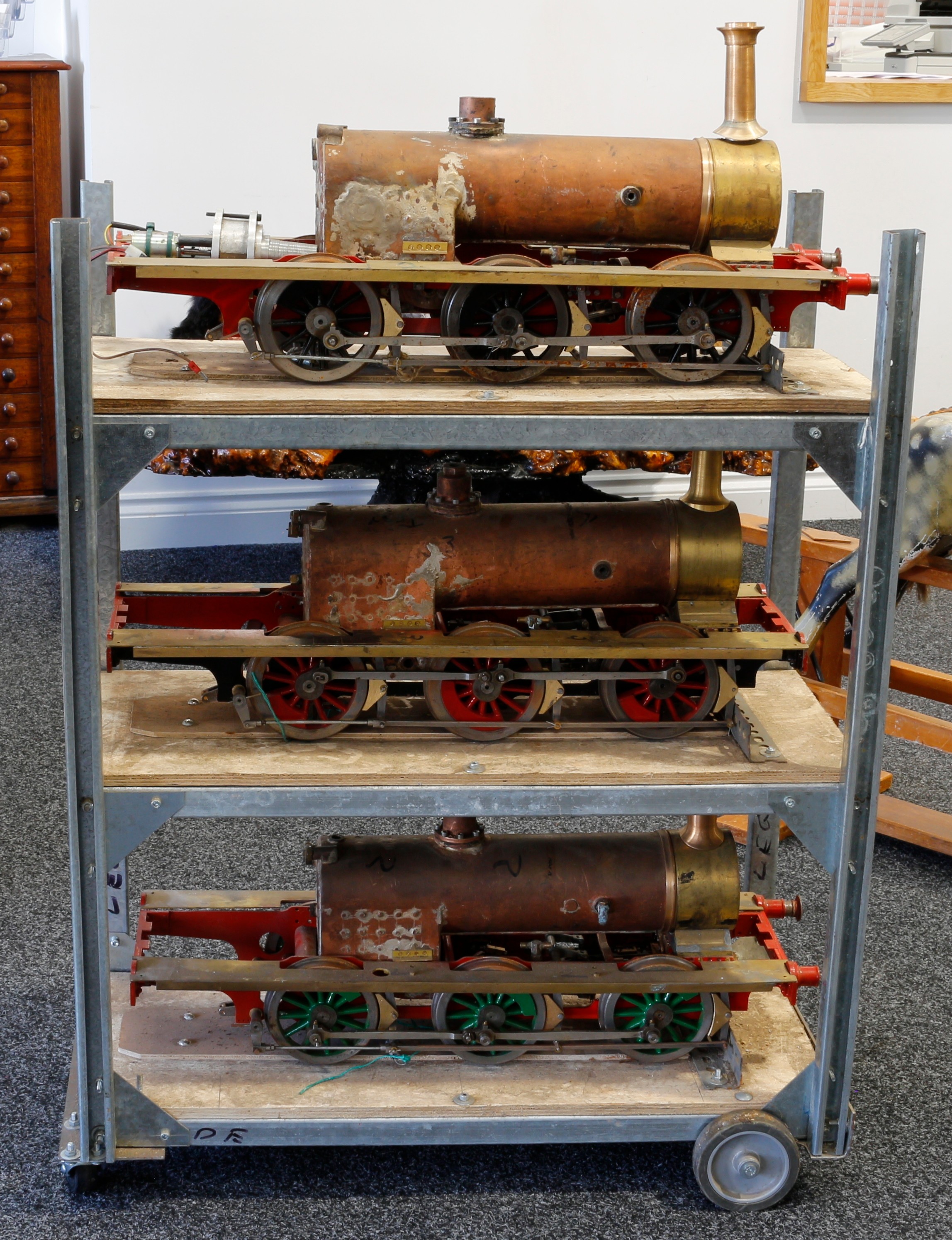 Live Steam and Model Engineering - a collection of three 5" gauge live-steam part built Terrier 0-6-0 tank locomotives, each approximately 67cm long, displayed with a three tiered bespoke display stand on wheels, 92cm high, 72cm wide, 33.5cm deep; the live-steam part built models accompanied with a box of loose parts, components and various technical scale drawings and plans (quantity)