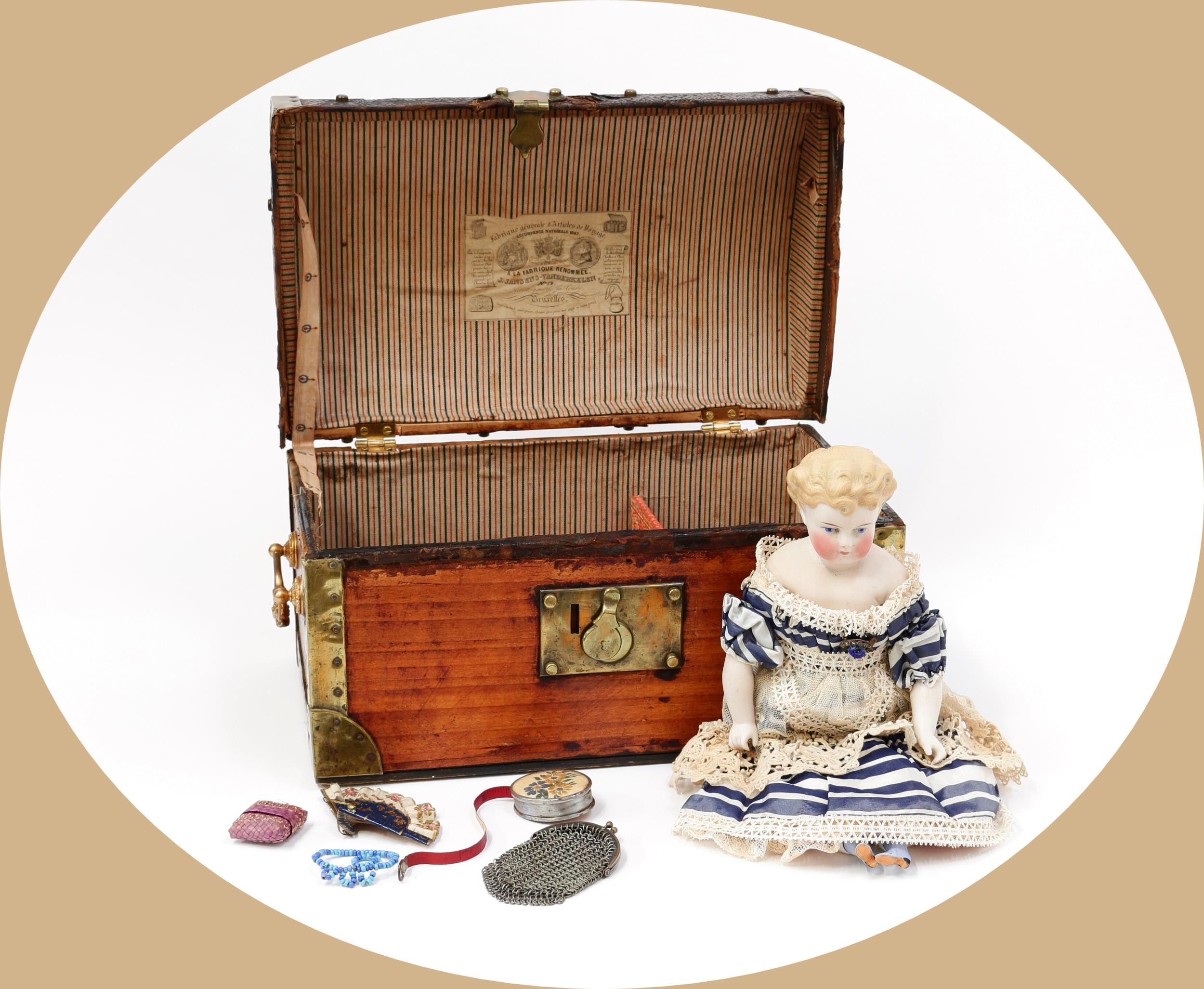 Toys From The Attic Part II - a 19th century unglazed Parian type shoulder head doll, the pale unglazed Parian type head with painted features including brown eyebrows, blue eyes, blush cheeks and red lips, moulded painted blonde hair, partially stuffed cloth body with unglazed bisque lower arms and lower legs with shaped boots, 32cm high; together with a rectangular shaped stained wooden and brass bound domed top travel trunk, the interior fitted with various doll accessories (quantity)