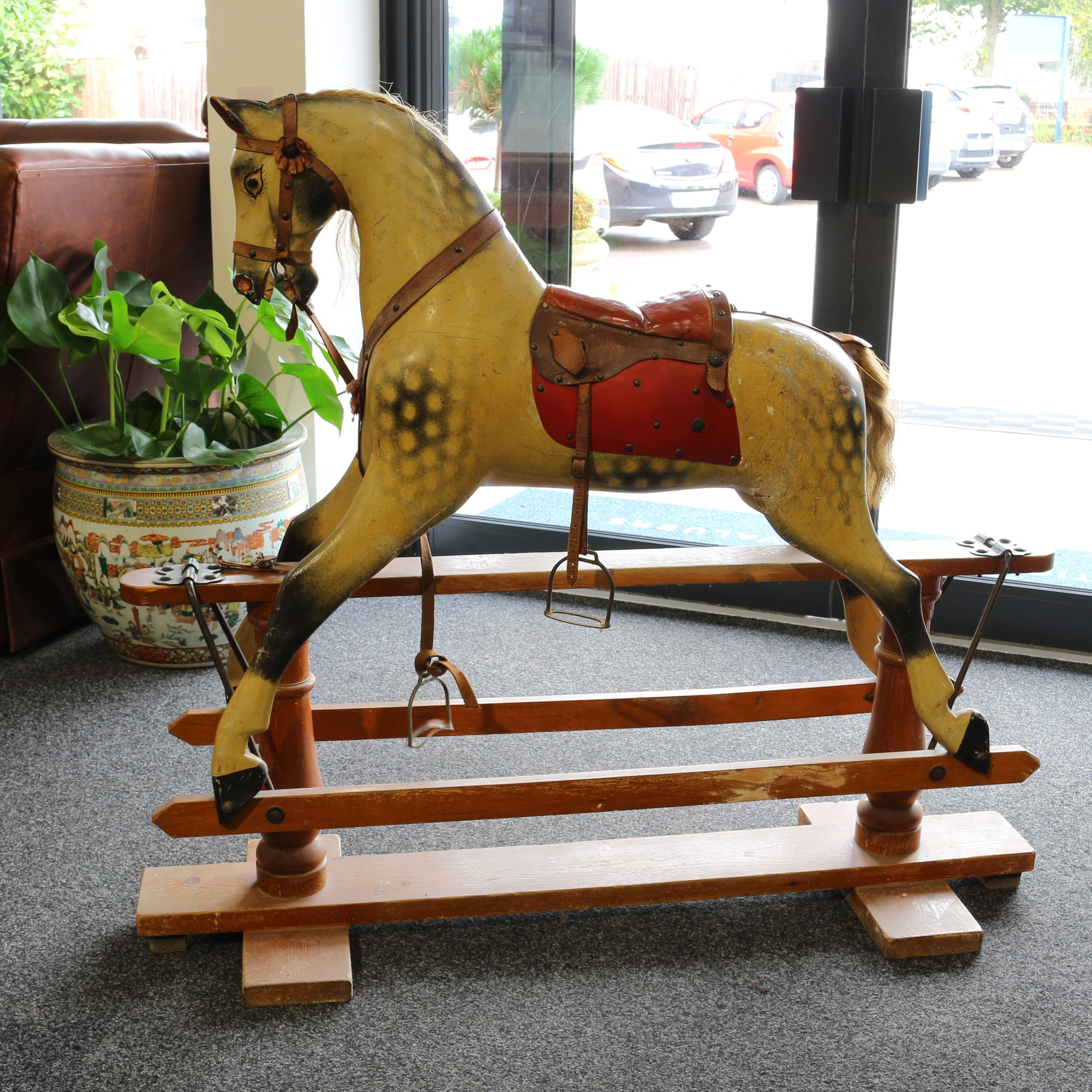 A late 19th century or early 20th century English wooden rocking Horse, the carved gesso and painted dappled Horse with pricked ears, flared nostrils and open mouth revealing teeth, the head inset with glass eyes with painted detail, oxblood red leather saddle, real horse hair mane and tail, the body with outstretched legs on swing stand, raised upon turned stand pillars and mounted with shaped brackets with four bolts applied to each, shaped pointed ends to side rails, 113cm high, 127cm long