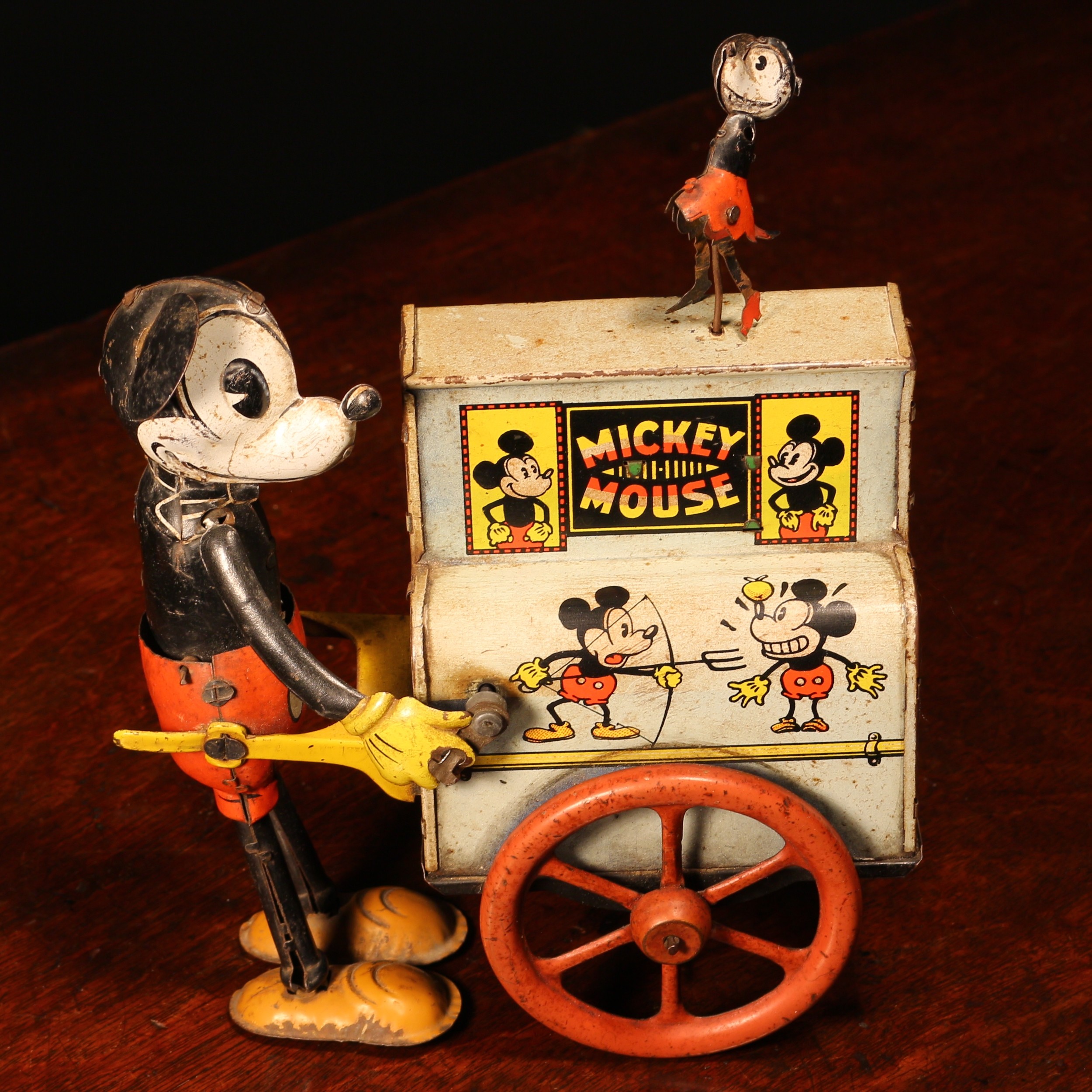 Walt Disney and Mickey Mouse Interest - a 1930's German novelty Mickey Mouse tinplate and fixed key wind mechanical toy, modelled as Mickey Mouse standing beside a barrel organ on wheels, the top of the barrel organ mounted with a miniature figure of Minnie Mouse, 20.5cm high, probably manufactured by Distler  For a similar example see Pressland, New Cavendish Books London, ISBN 0 904568 04 0, page 140, item number 400.
