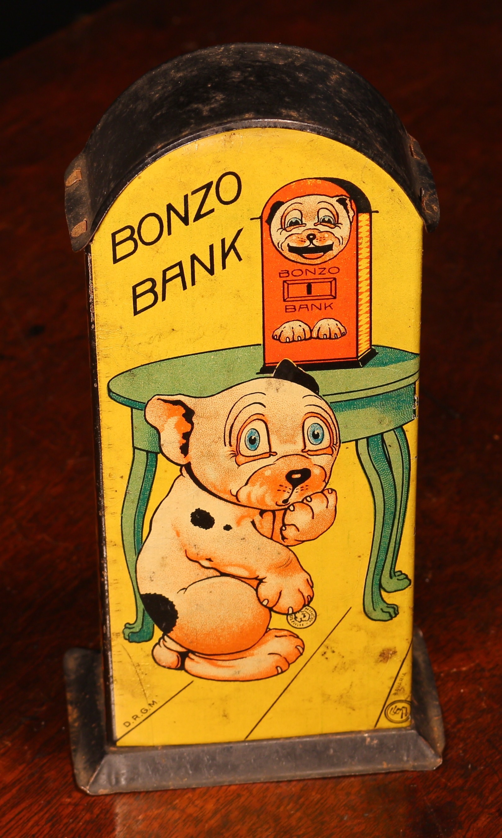 A 1920's/1930's tinplate novelty lever action mechanical money box or bank, Bonzo Bank, lithographed detail, modelled as Bonzo the Dog, 'BONZO BANK, PRESS THE LEVER LIGHTLY, WATCH MY TONGUE APPEAR, SAVE A PENNY NIGHTLY, MAKE YOUR FORTUNE HERE.', manufactured by Saalheimer & Strauss, 18cm high