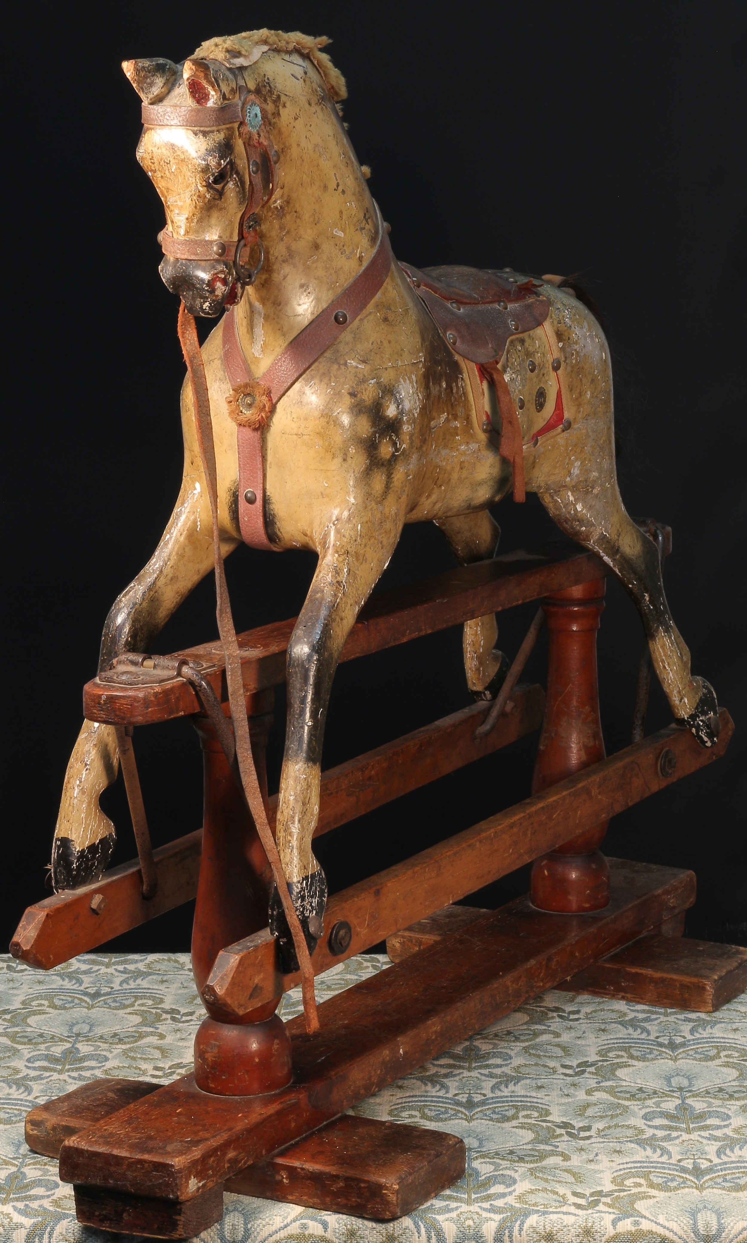 A late 19th century English wooden rocking Horse, of small proportions, attributed to Frederick Henry Ayres (F H Ayres, London), the carved, gesso and painted dappled Horse with pricked ears, flared nostrils and open mouth, the head inset with amber and black glass eyes, brown tan leather saddle, real horse hair tail, the body with outstretched legs on swing stand, raised upon a pair of turned stand pillars and mounted with shaped rectangular brackets with three bolts applied to each, trademark side rails with shaped pointed ends, 79cm high, 81cm long