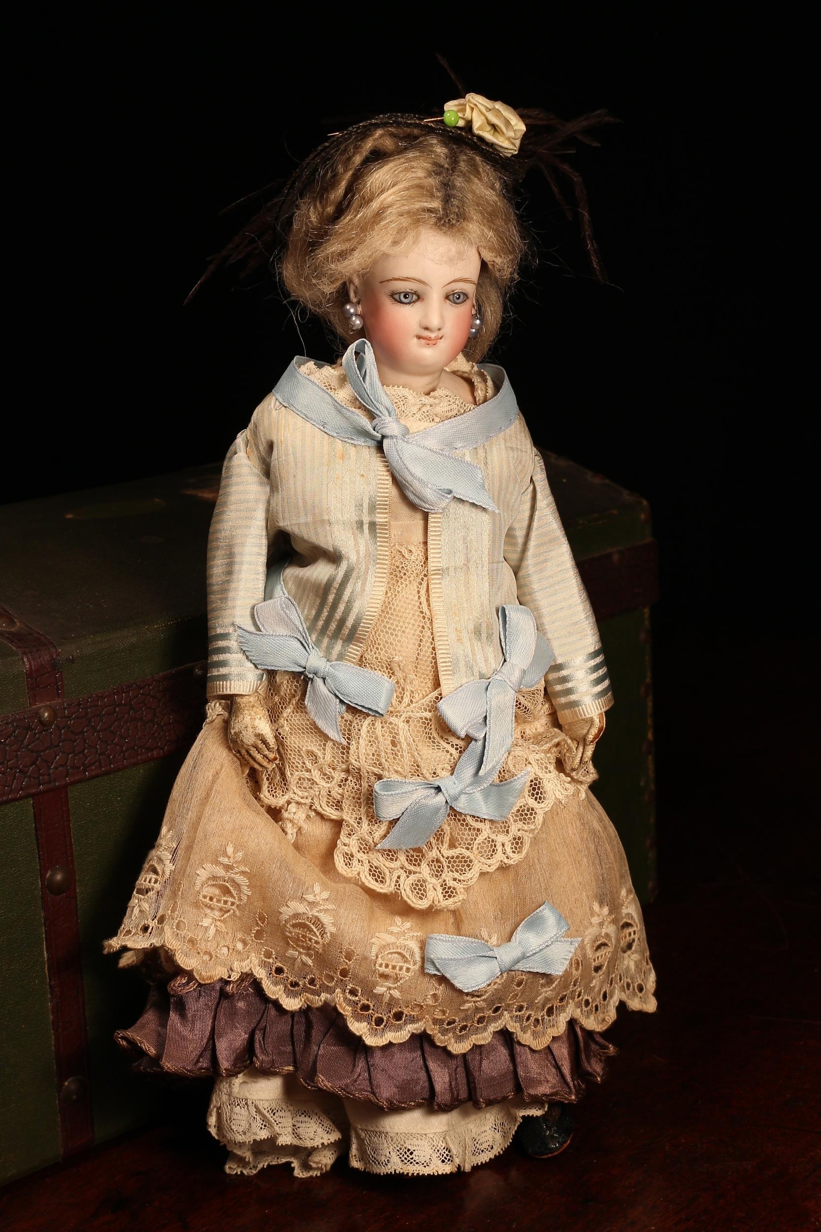 A 19th century Bru Jne & Cie (France) bisque shoulder and bisque head French Poupée de Mode or fashion smiling doll, the bisque head inset with fixed blue glass eyes, painted features including brown feathered eyebrows, fine eyelashes, red lips and red blush cheeks, blonde wig on pate, pierced ears, partially stuffed cloth body with white kid leather arms, impressed mark 'A', 28cm high; together with a green canvas covered rectangular shaped domed top travel trunk, the interior fitted with a lift out tray with various doll clothing, accessories and miniatures (quantity)