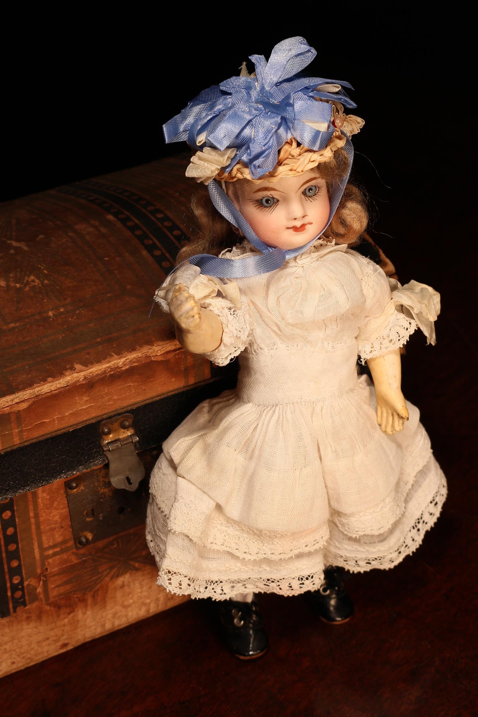 A late 19th century French bisque head Bébé doll, of small proportions, the bisque head with inset fixed blue glass eyes, painted features including thick brown eyebrows, fine eyelashes, red lips and blush red cheeks, blonde wig on pate, jointed painted composition body, impressed marks 'PARIS, J 0 D', 23cm high; together with a paper covered rectangular shaped domed top travel trunk, the interior fitted with a single lift out tray with various doll clothing, miniature novelties and accessories (quantity)