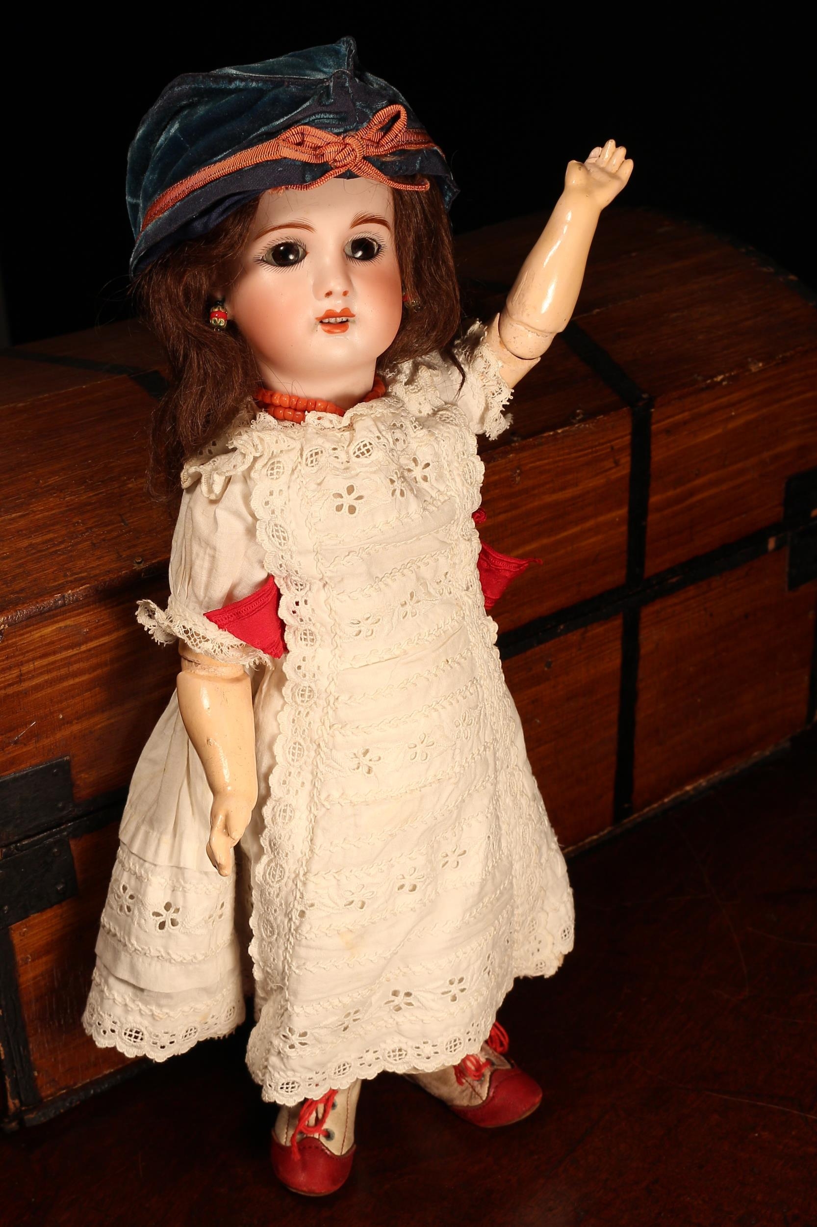 An S.F.B.J. (Société Francaise de Fabrication de Bébé & Jouets, France) bisque head and painted composition bodied Bébé doll, the bisque head with weighted sleeping brown glass eyes, painted features including feathered brown eyebrows, fine eyelashes and red lips, partially open mouth revealing upper teeth, brown wig on pate, pierced ears, impressed marks 'S.F.B.J., PARIS., 4', 35.5cm high; together with a rectangular shaped wooden travel trunk, the interior fitted with a single lift out tray wi