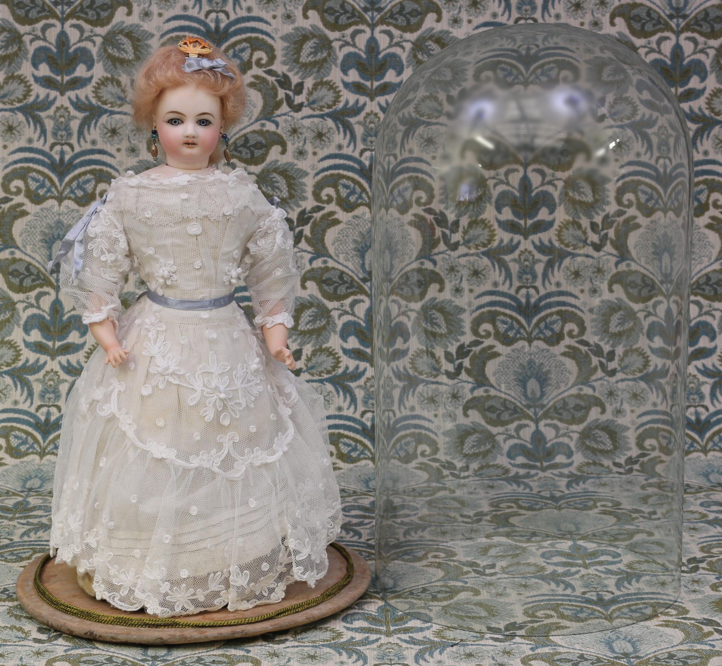 A French bisque head and bisque shoulder plate waltzing automaton doll, attributed to Jules Nicholas Steiner (France), the bisque head with fixed blue glass eyes, painted features including feathered brown eyebrows and fine eyelashes, open mouth revealing teeth, blonde wig on cork pate, pierced ears, unmarked, the upper torso in kid leather, bisque lower arms, carton covered lower body, fixed key wind mechanism with lever, 39cm high; displayed under a glass display dome with circular wooden plinth base