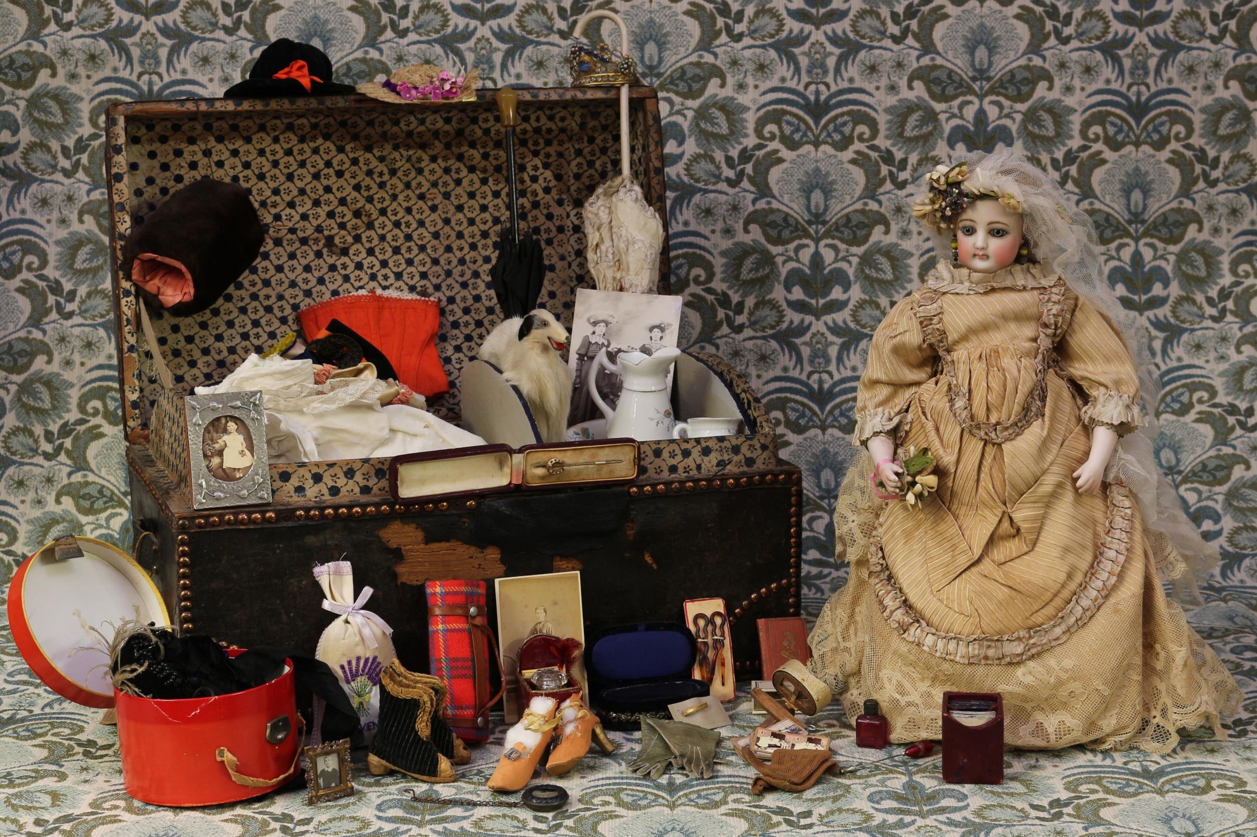 A 19th century pale bisque head French Poupée de Mode or fashion doll, attributed to Francois Gaultier, the bisque head inset with fixed blue glass eyes and painted features including brown feathered eyebrows, fine eyelashes, red lips and large blush cheeks, blonde wig on pate, pierced ears, kid leather body with bisque lower arms, impressed mark '4.', 42cm high; together with a copper studded domed top leather-bound trunk, of small proportions, carrying handles to sides, 25cm high, 46cm wide, 27cm deep, the interior partially fitted with various doll clothing, accessories and miniatures