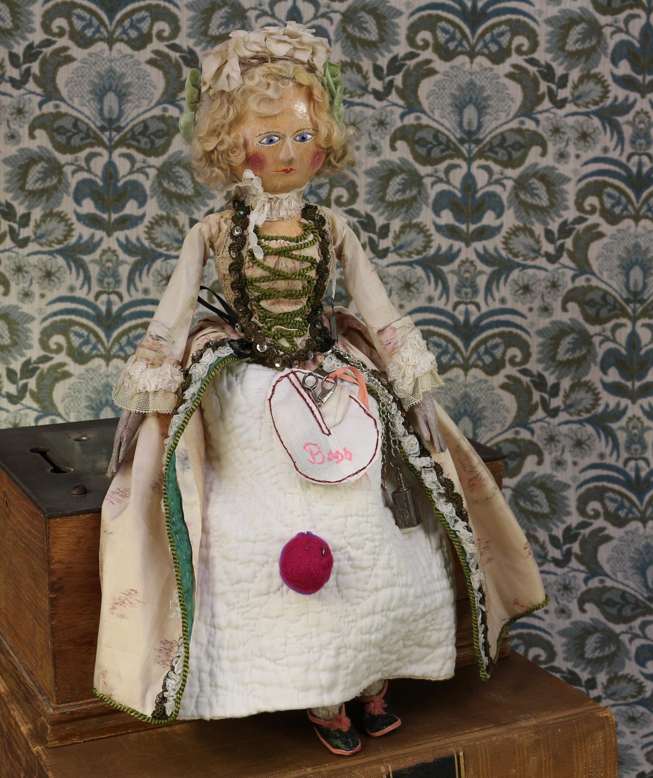 A late 18th century 'Queen Anne' type English carved and painted wooden doll, the carved and painted head inset with blue glass eyes, painted features including thin eyebrows, red lips and blush cheeks, blonde wig attached with nails, carved and painted wooden torso, kid leather forearms and hands, 38cm high