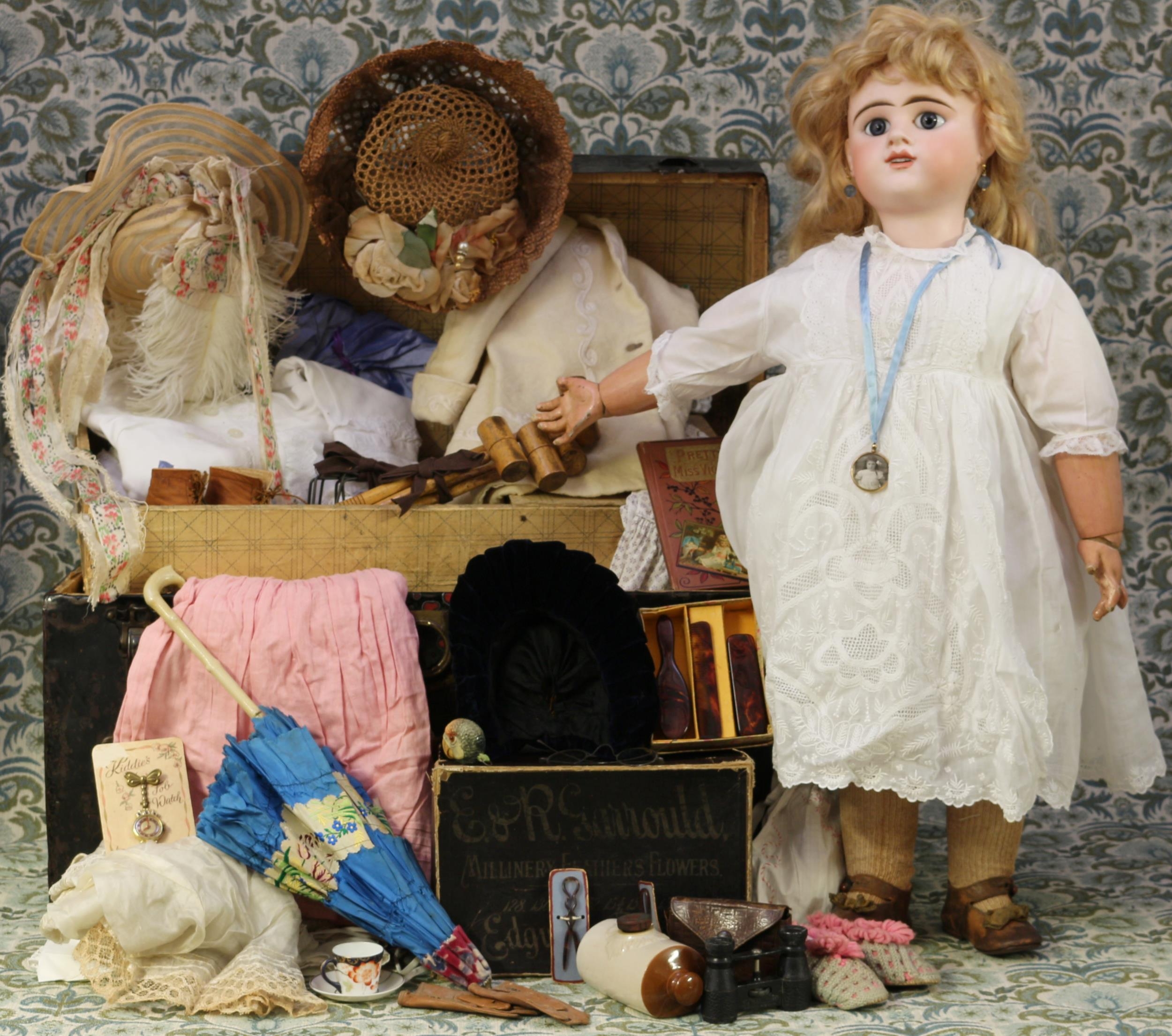 An Etienne Denamur (France) bisque head and painted composition bodied Bébé doll, the bisque head with inset fixed blue glass eyes, painted features including large brown feathered eyebrows and fine eyelashes, open mouth revealing teeth, pierced ears, blonde wig on pate, impressed marks 'E.13.D DEPOSE', 73cm high; together with a domed top steamer trunk, the fitted interior with lift out tray and compartment containing various doll clothing, accessories and novelties including a miniature croquet set, a Lovatt's Langley Ware miniature salt-glazed hot water bottle etc (quantity)