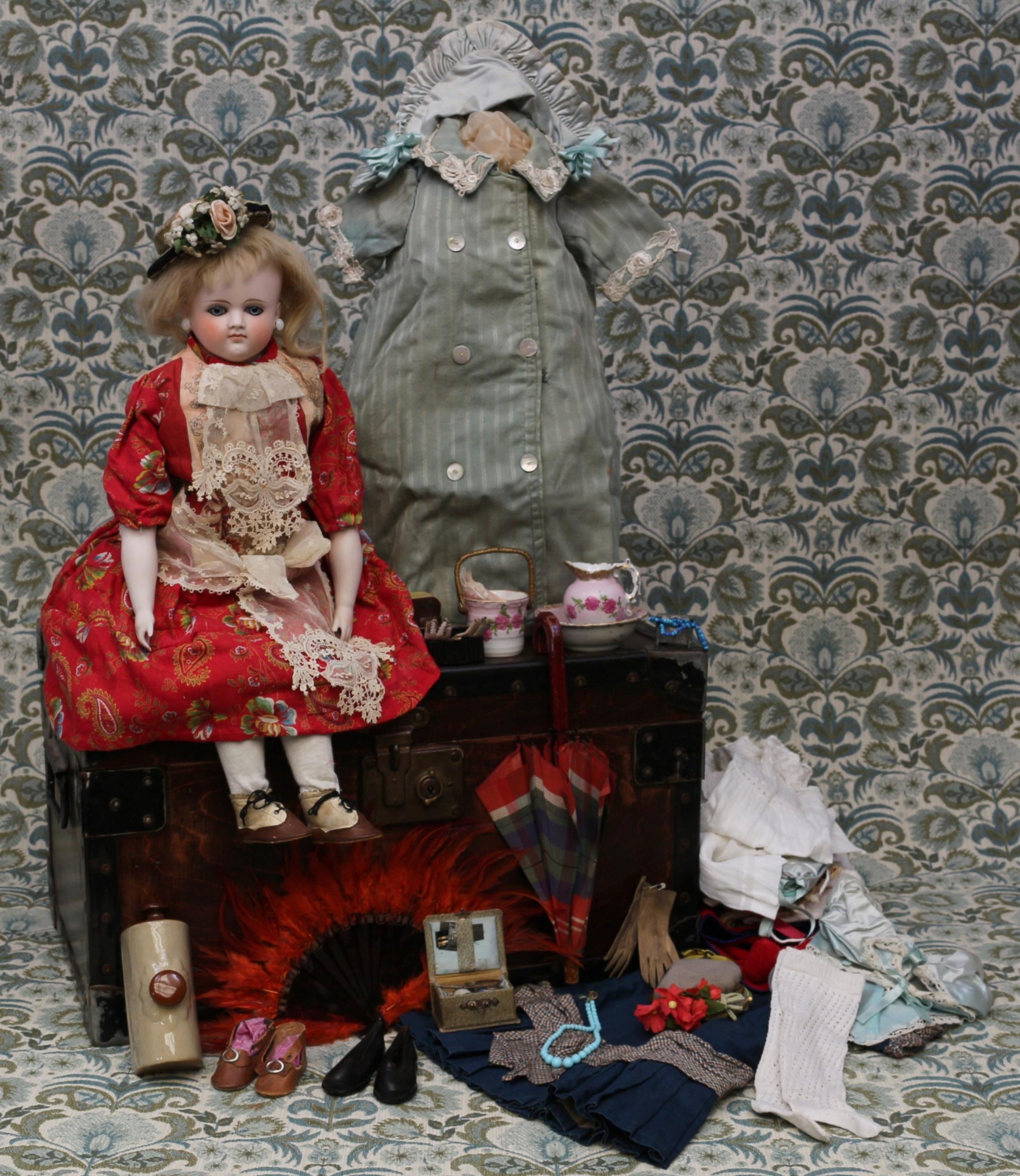 A 19th century pale bisque shoulder head French Poupée de Mode or fashion doll, the bisque head inset with fixed blue glass eyes and painted features including brown feathered eyebrows, fine eyelashes, red lips and blush cheeks, blonde wig on pate, pierced ears, kid leather body with bisque lower arms, impressed mark '11', 51cm high; together with a rectangular shaped wooden travel trunk, of small proportions, 28cm high, 51cm wide, 32cm deep, the interior partially fitted with various doll clothing, accessories and miniatures (quantity)