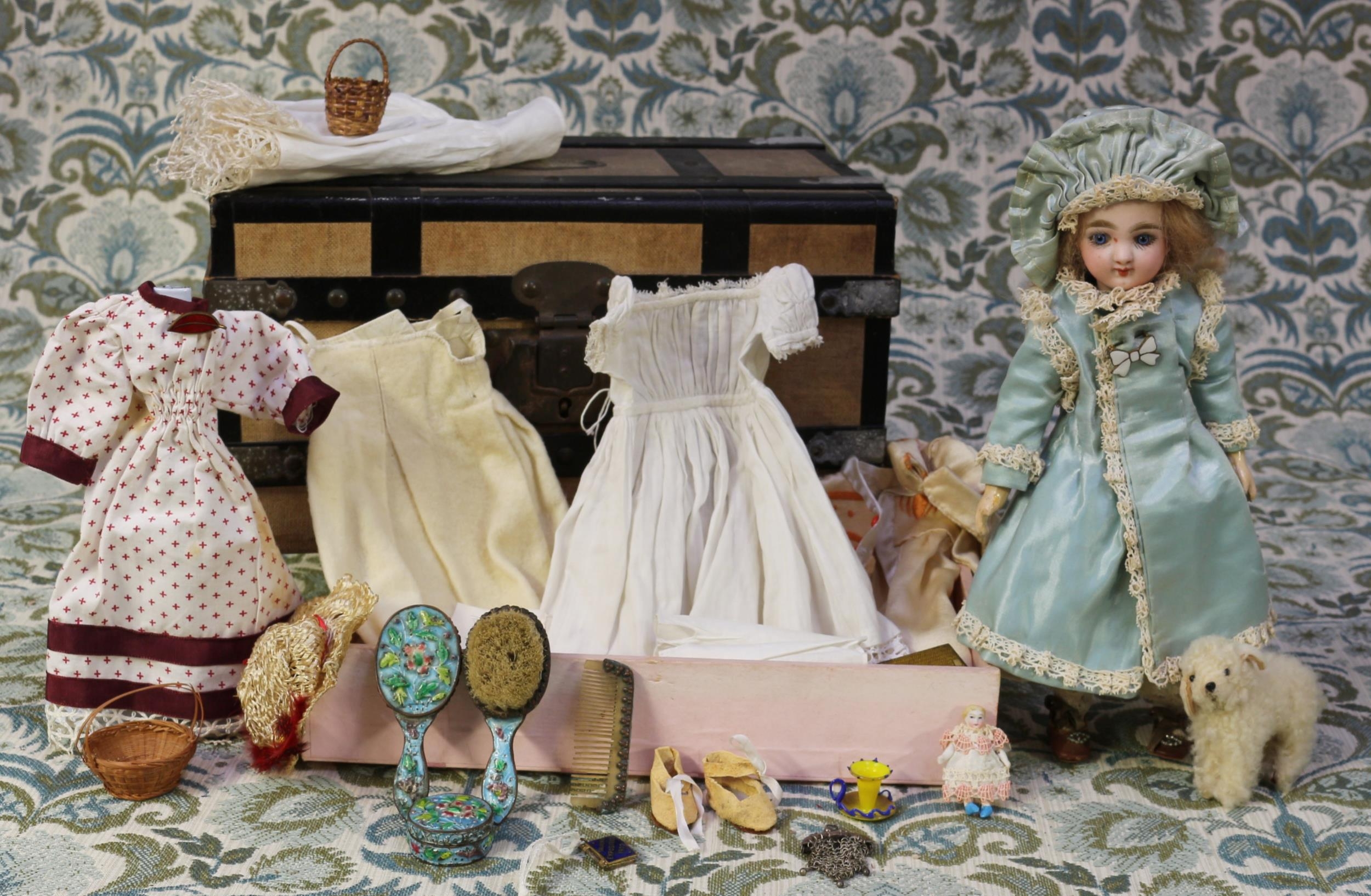 A Fleischmann & Bloedel bisque head Eden Bébé doll, the bisque head with fixed blue glass eyes, painted features including brown feathered eyebrows and fine eyelashes, red lips, blonde wig on a cork pate, impressed marks 'EDEN PARIS D', 25cm high; together with a linen bound rectangular shaped trunk of small proportions, carrying handles to sides, 16cm high, 29cm wide, 17cm deep, the fitted interior with lift out tray, with various doll clothing, accessories and miniatures