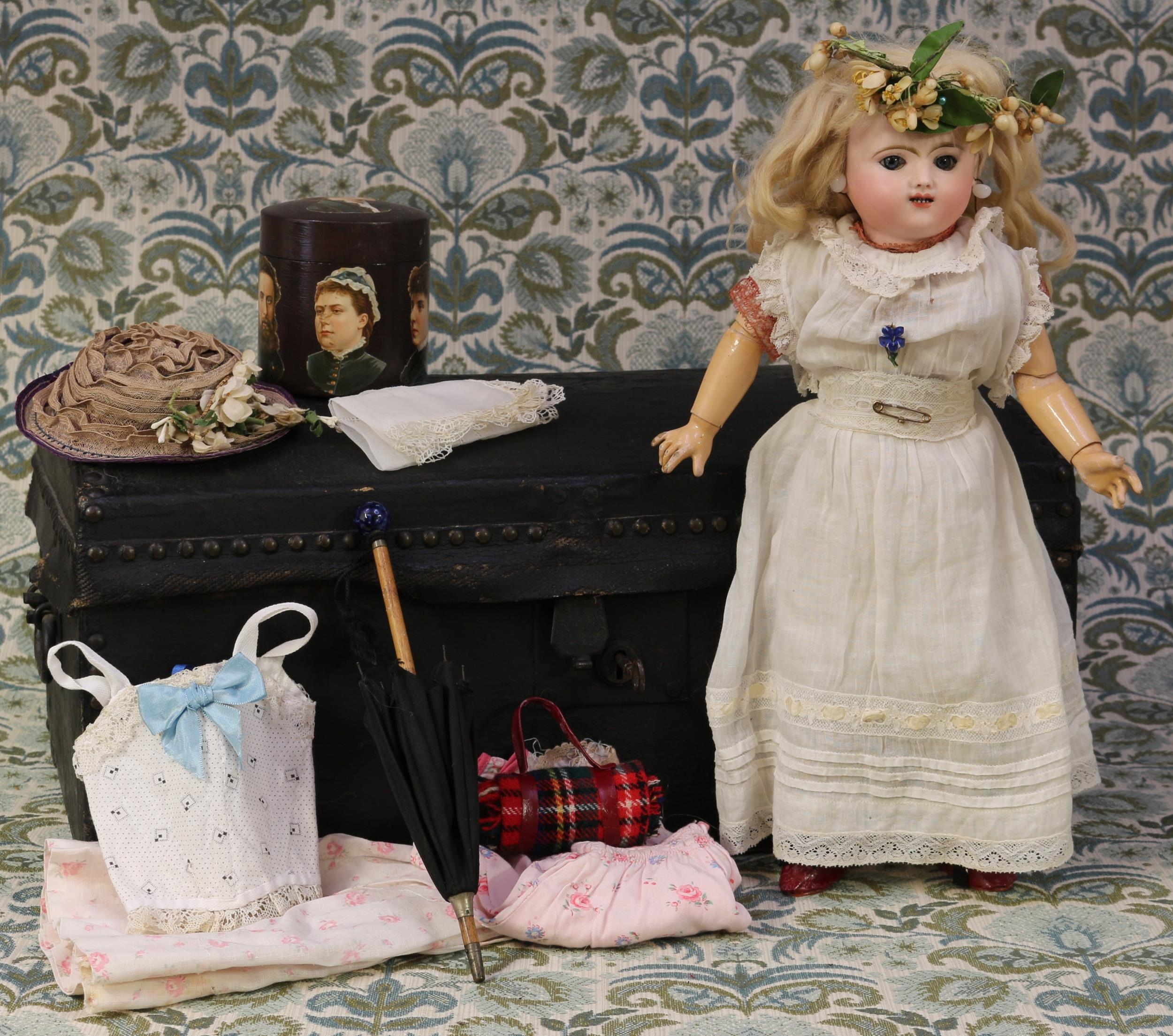 A French bisque head Bébé doll, attributed to Jules Nicholas Steiner (France), the bisque head with fixed blue glass eyes, painted features including brown feathered eyebrows and fine eyelashes, open mouth revealing teeth, blonde wig on pate, pierced ears, the head unmarked, 'SFBJ, FABRICATION FRANCAISE PARIS' circular label to the reverse of the torso, 41cm high; together with a brass studded domed top leather-bound trunk, of small proportions, iron handles to sides, 24cm high, 50cm wide, 30.5cm deep, the interior fitted with various doll clothing and accessories including a black cotton doll's parasol etc