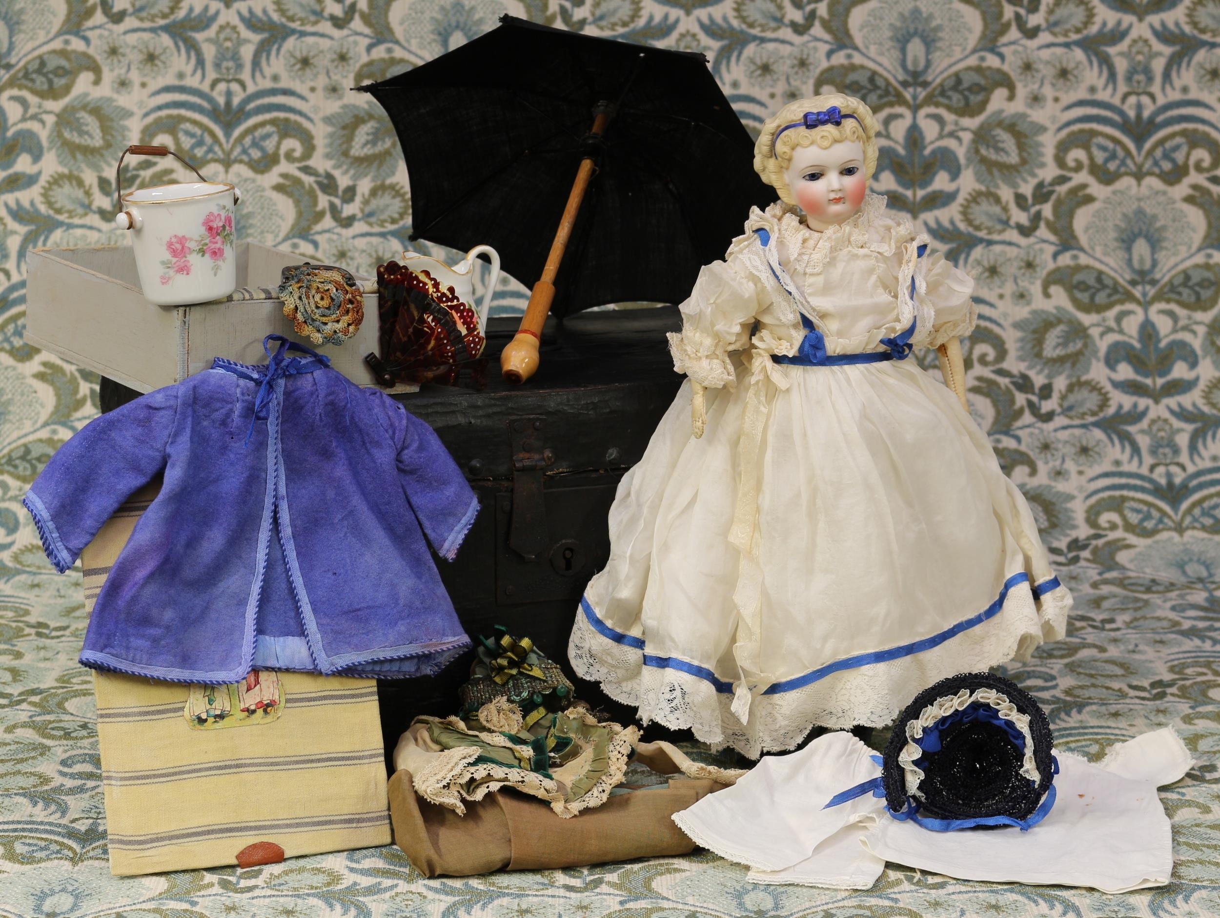 A 19th century unglazed Parian type swivel neck doll, unmarked but attributed to Simon & Halbig (Germany), the unglazed head with moulded blonde hair and blue bow, inset blue glass eyes and painted features including brown feathered eyebrows, fine eyelashes, rid lips and large blush cheeks, unglazed Parian type torso with kid leather arms, partially stuffed cloth body, 34cm high; together with a painted linen bound rectangular shaped trunk of small proportions, carrying handles to sides and handle to lid, 20cm high, 36cm wide, 22cm deep, the partially fitted interior with lift out section, with various doll clothing, accessories and miniatures
