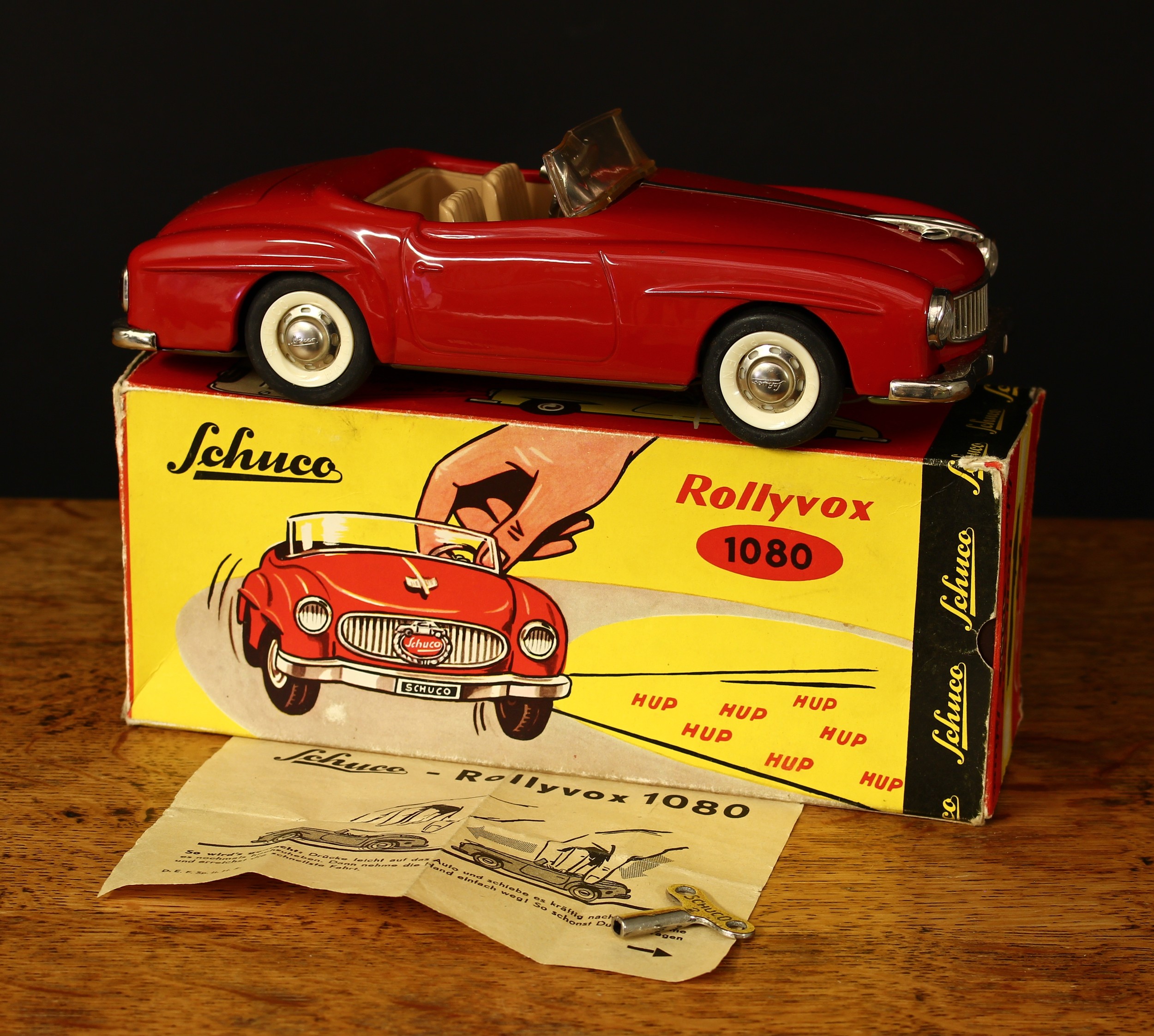 A Schuco (Germany) tinplate friction driven Rollyvox 1080 open top car, red body with beige/tan interior, novelty horn operation, boxed with original clockwork key and original operating instructions slip
